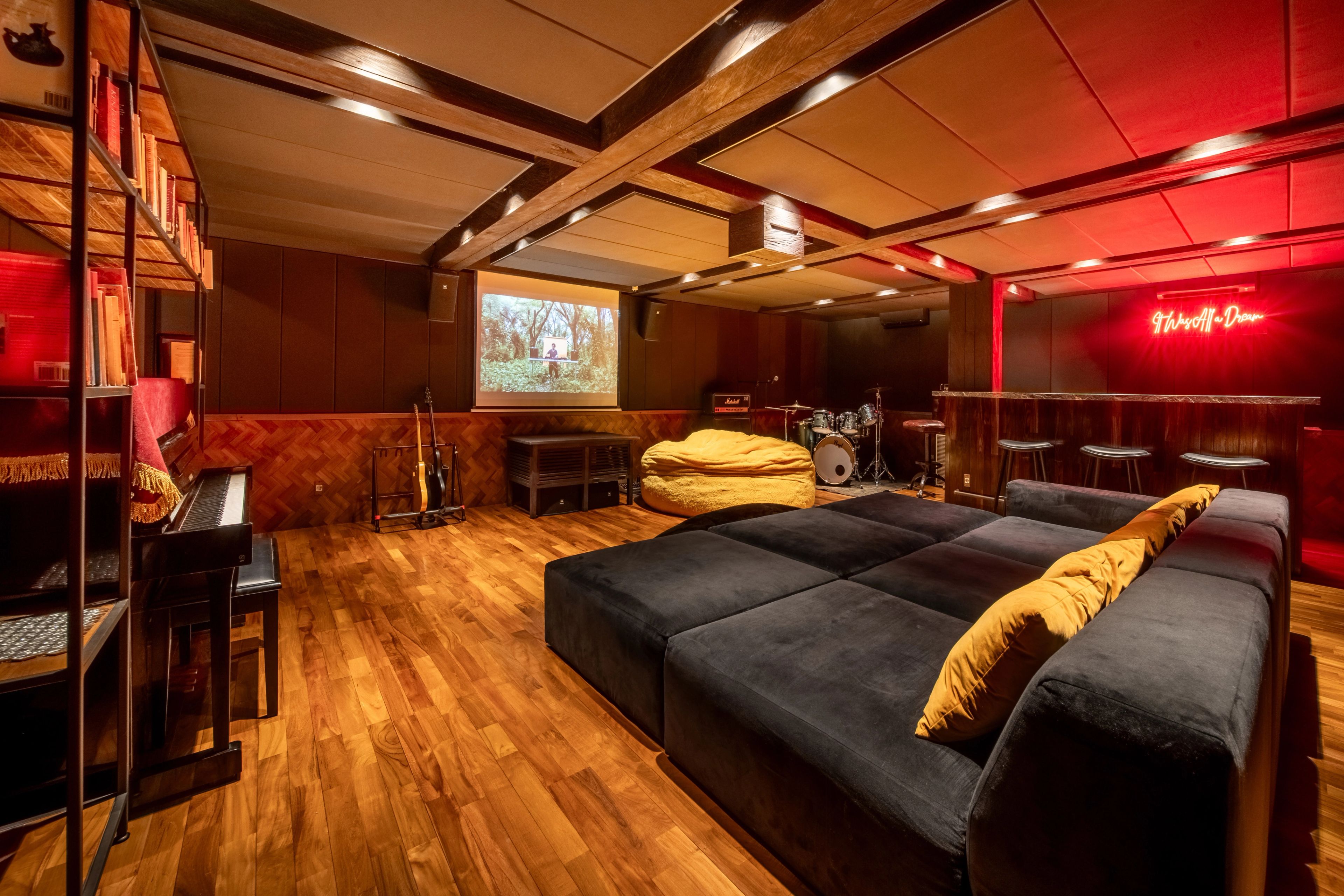 The basement's cinema seating and screen under red light, drum kit and bar along the far wall.