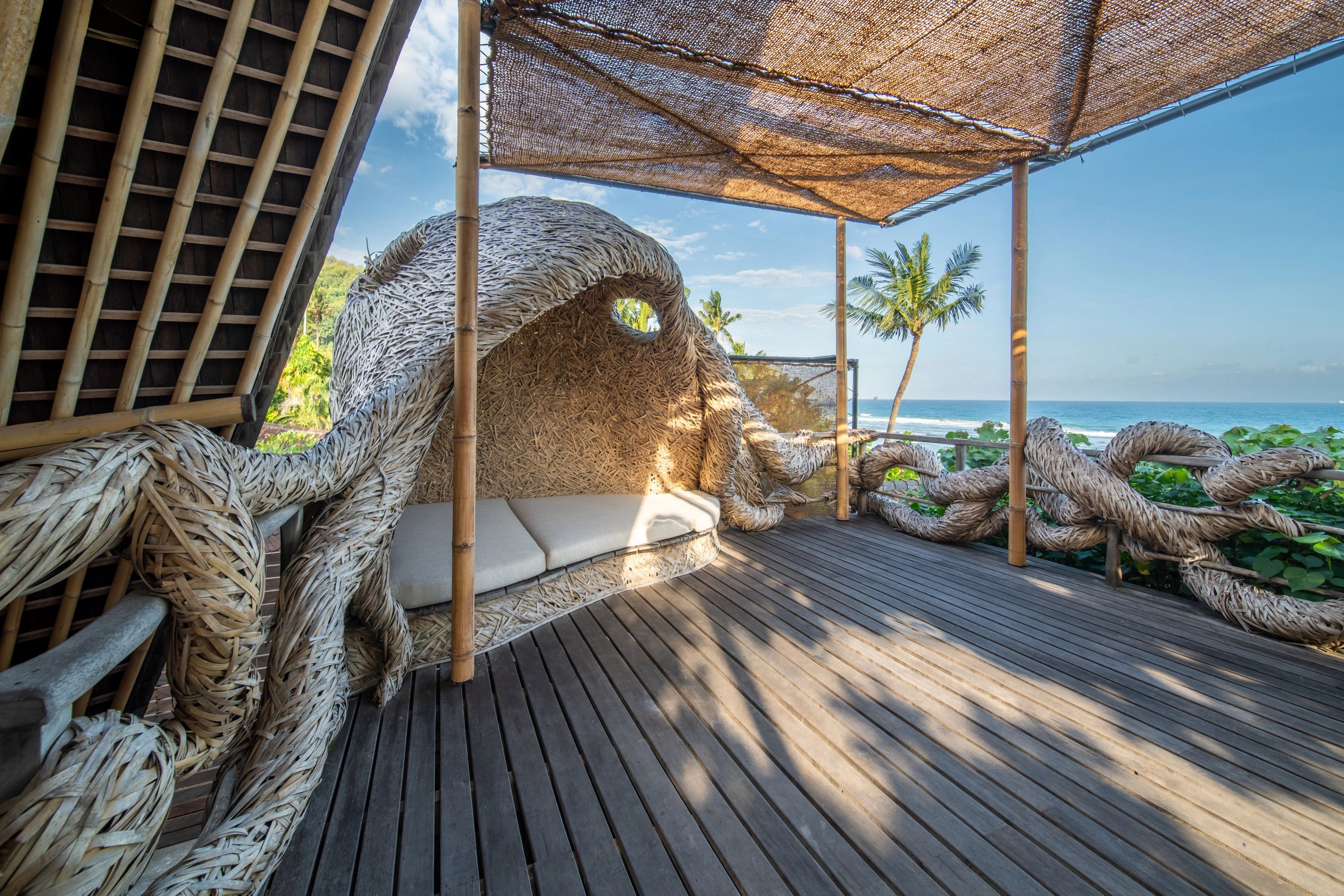 A cushioned daybed in the sculpted alcove, its woven rope forms spilling along the deck rail.