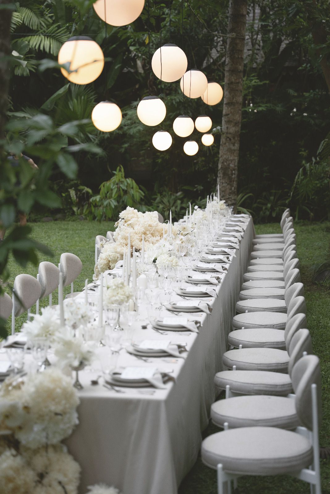 A white tablescape running the length of the table, candlesticks and dense white flowers along its centre.