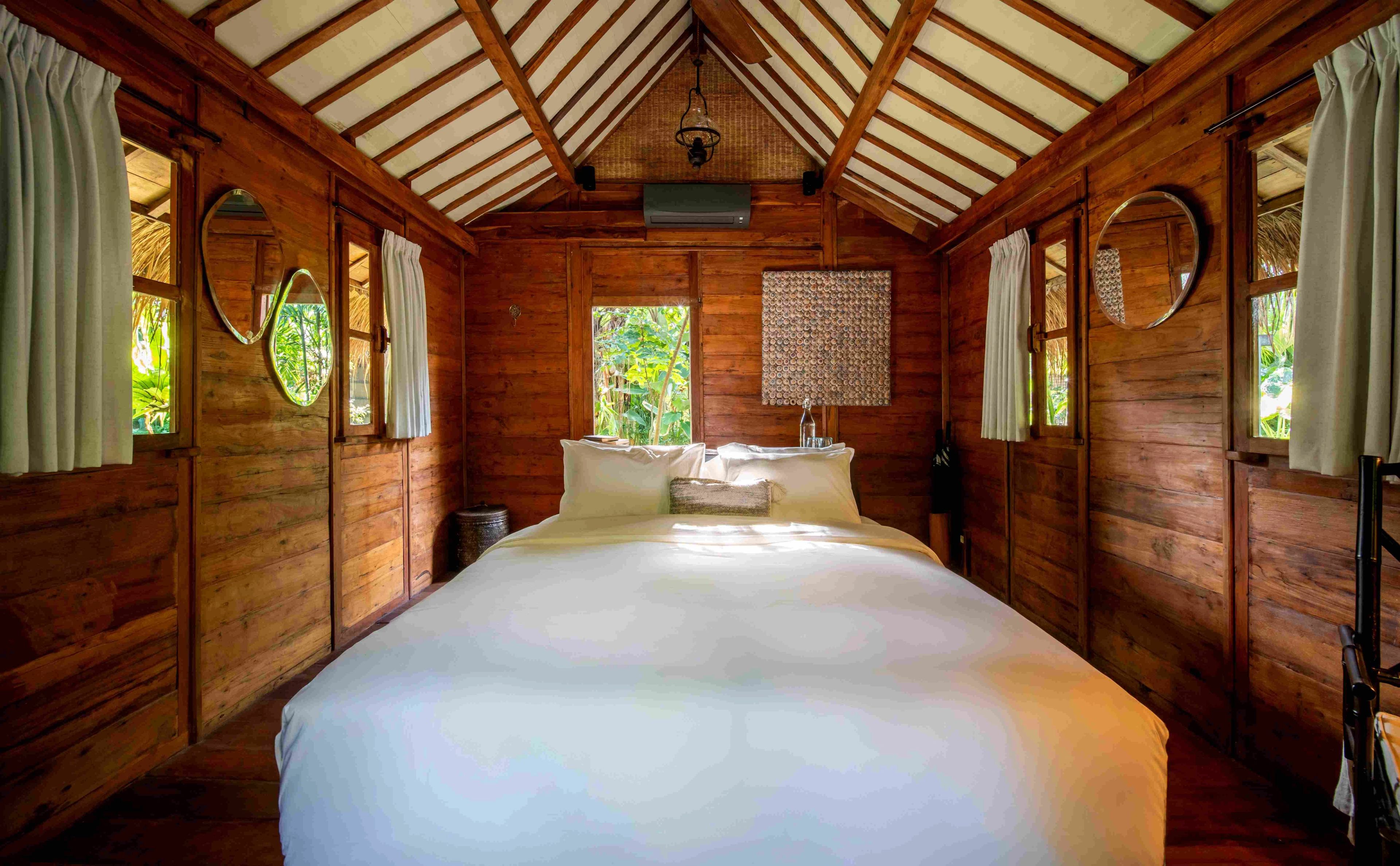 A wide bed in the timber-panelled bedroom, under an exposed pitched roof with round porthole windows either side.