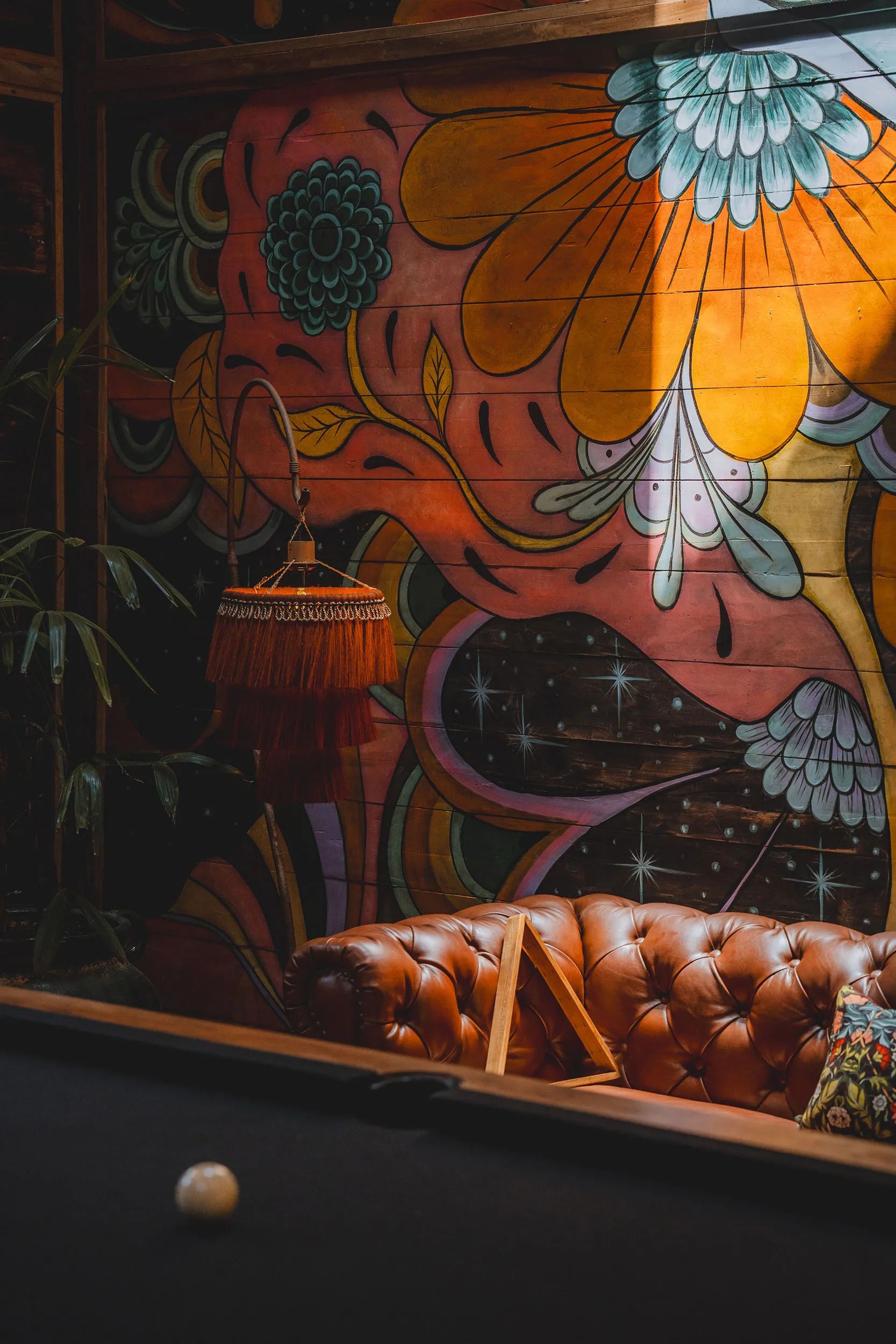 A tasselled pendant lamp and a leather chesterfield against a brightly painted mural.