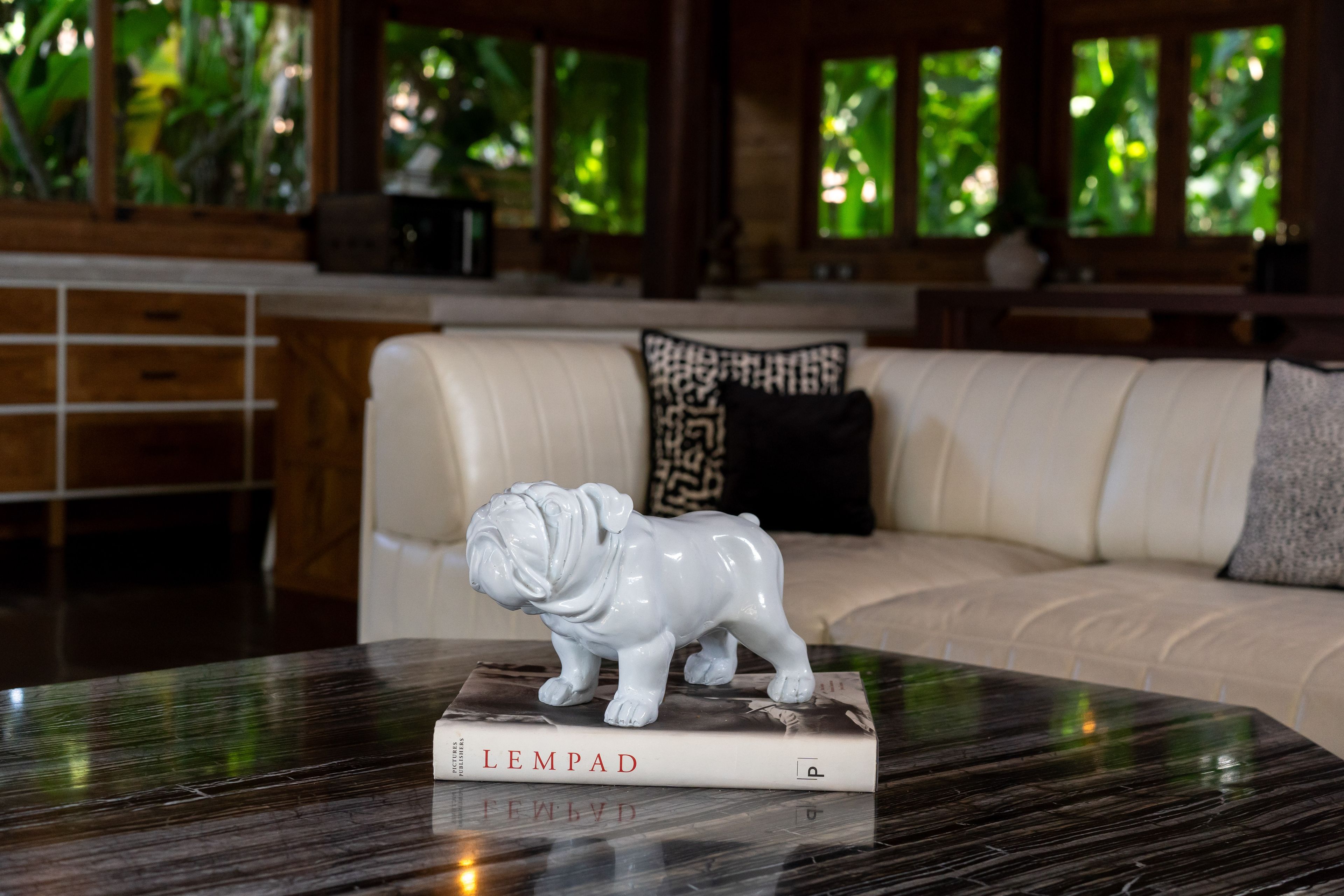 A white ceramic bulldog on a stack of books on the coffee table, sofa behind.