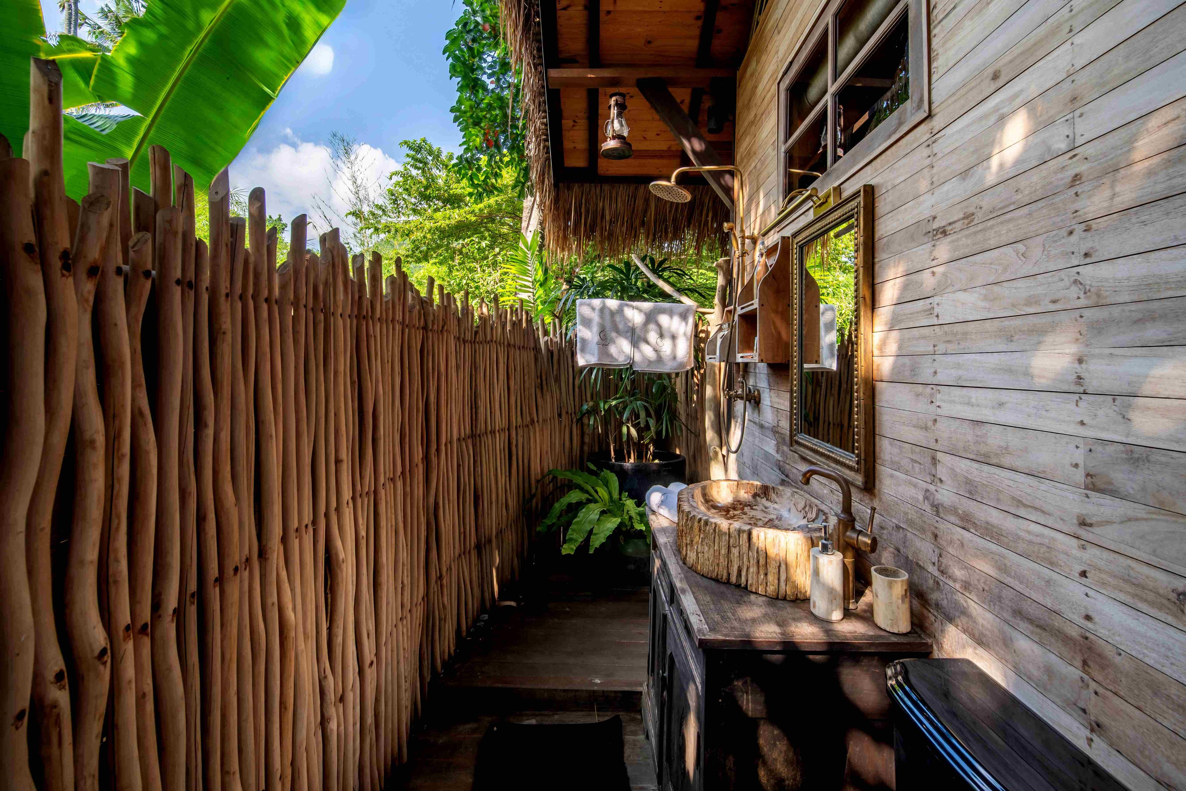 A driftwood screen enclosing the outdoor bathroom, with a basin and lantern against the timber wall.