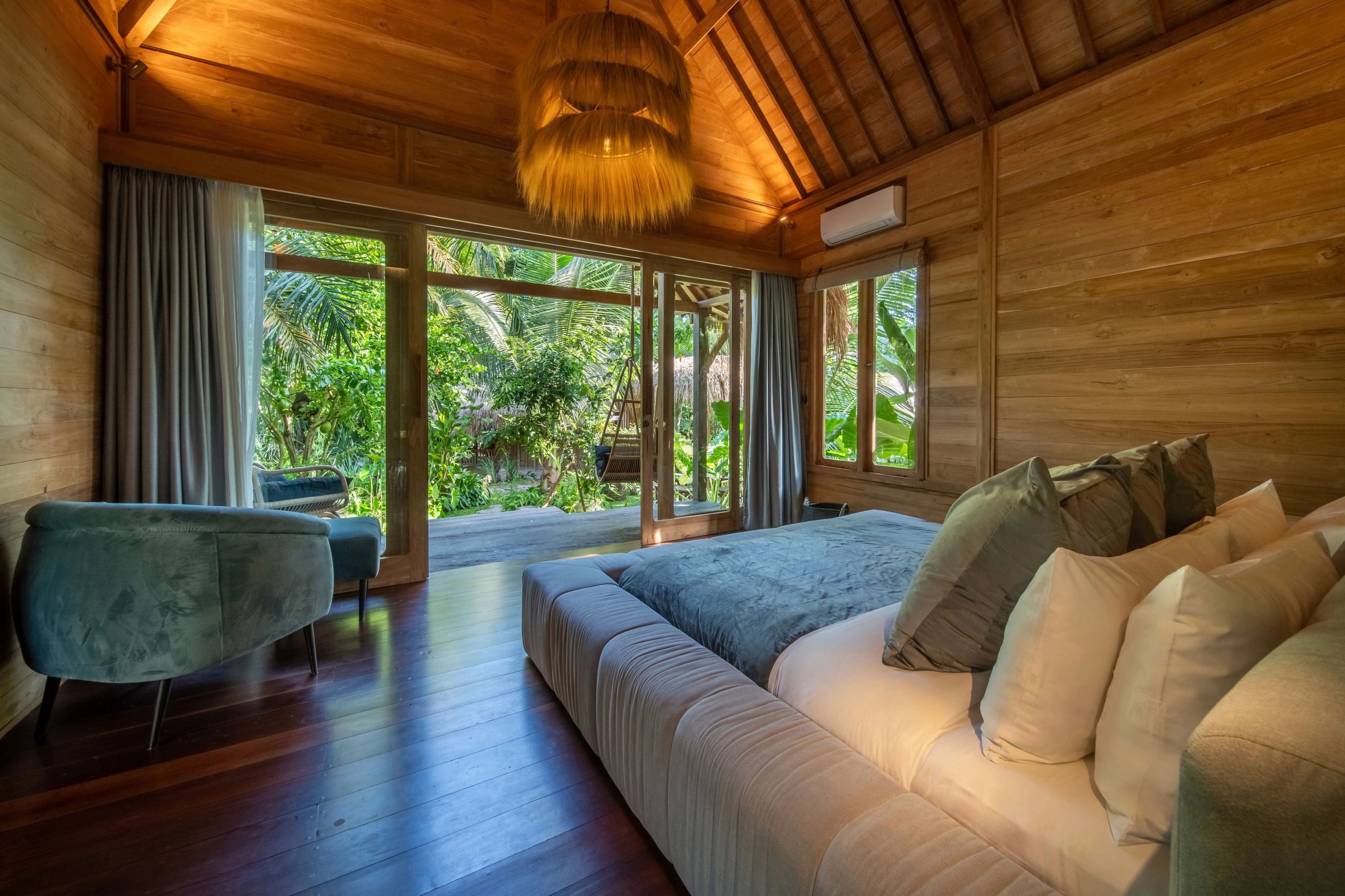 A long sofa and armchair in the bedroom under a woven pendant, windows to the garden.
