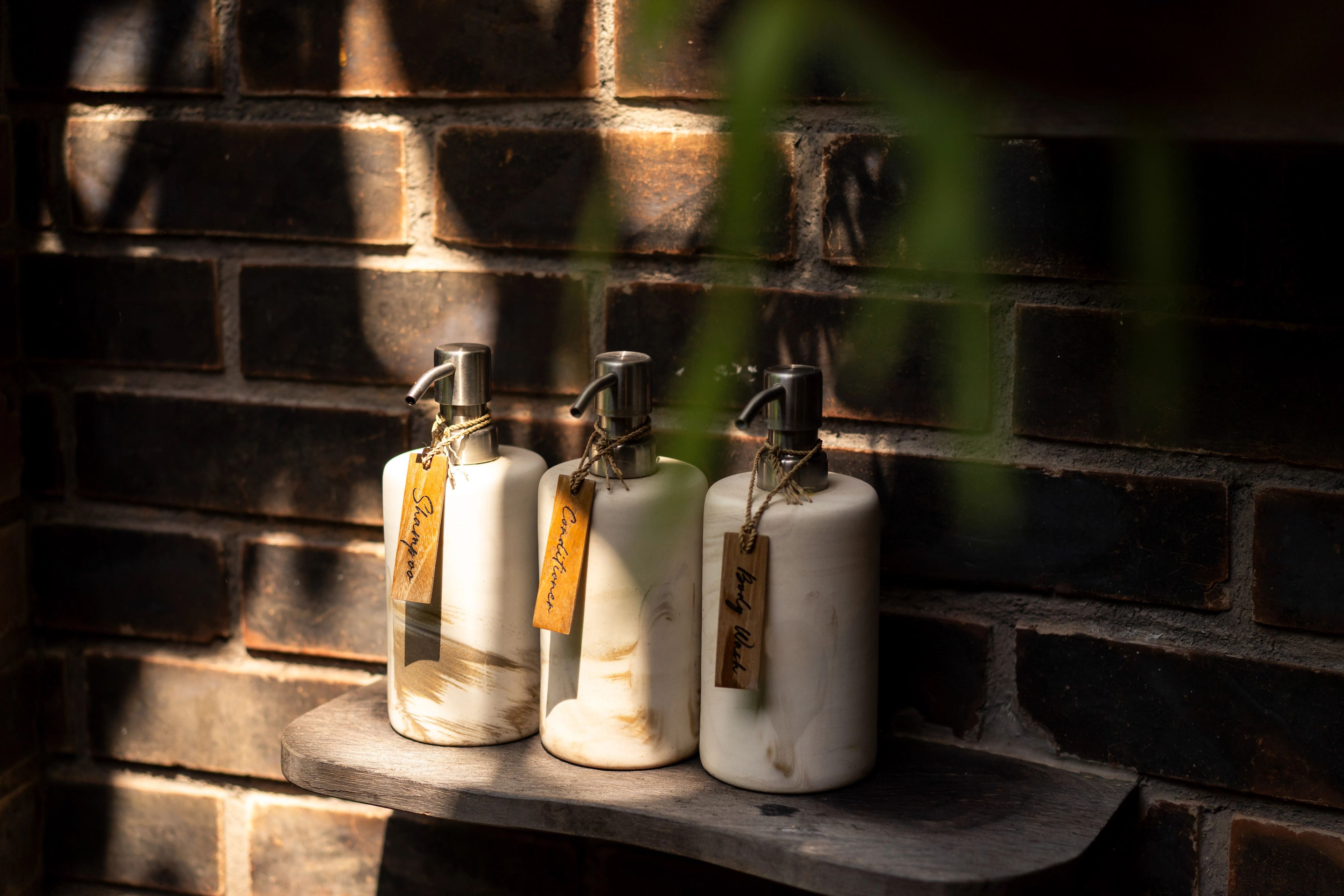 Three ceramic amenity bottles on a stone shelf against a dark brick wall.