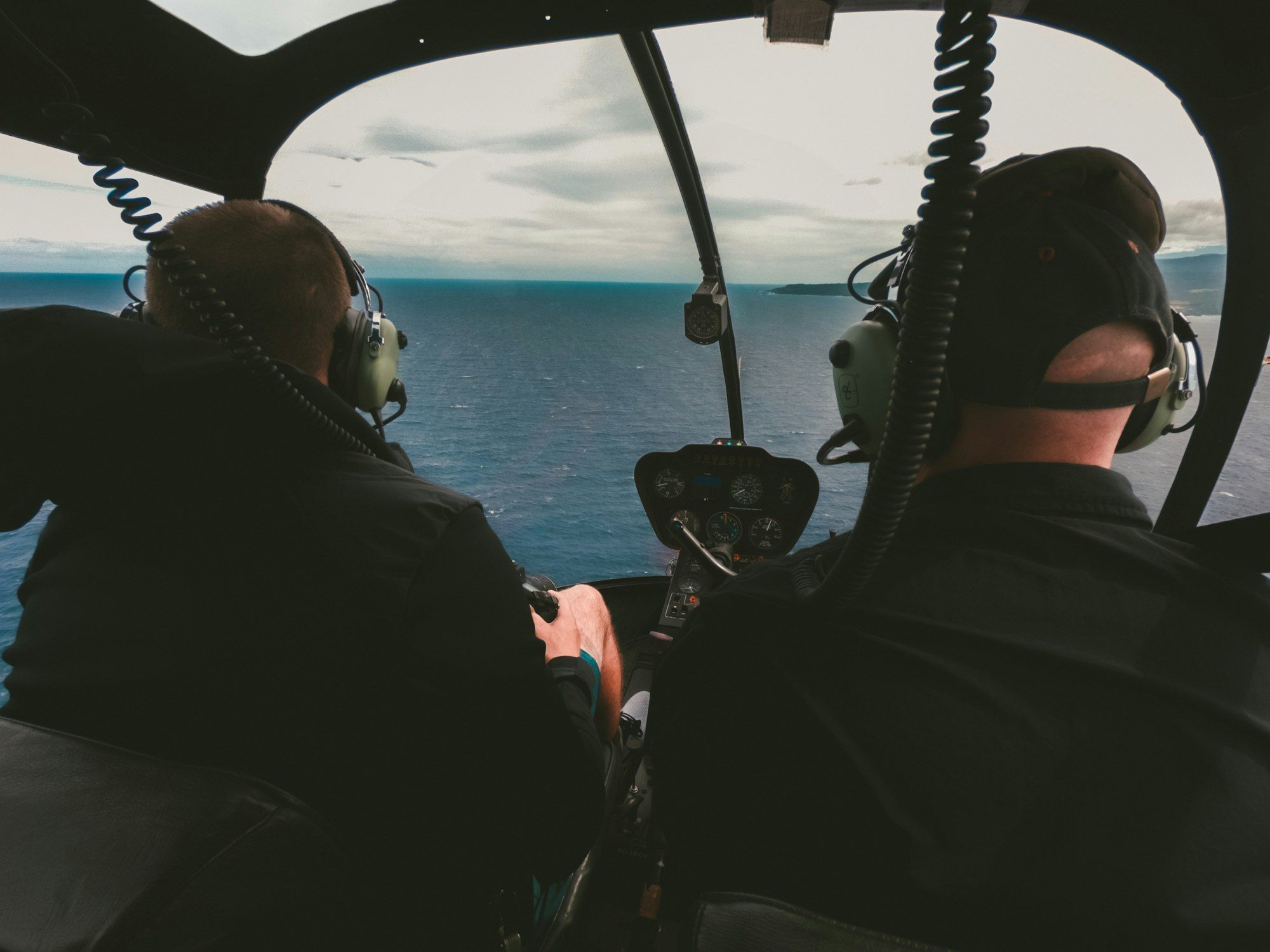 Two passengers in a helicopter cabin over the sea in low light