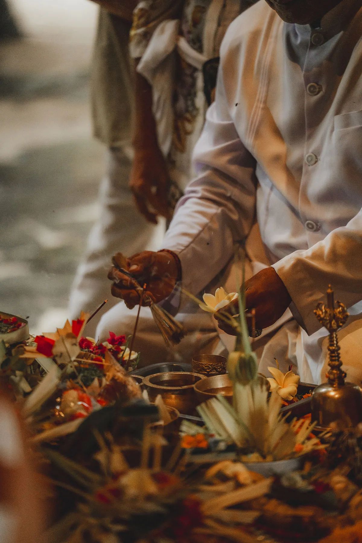 A priest's hands ringing a bell over flower offerings laid out on brass trays.