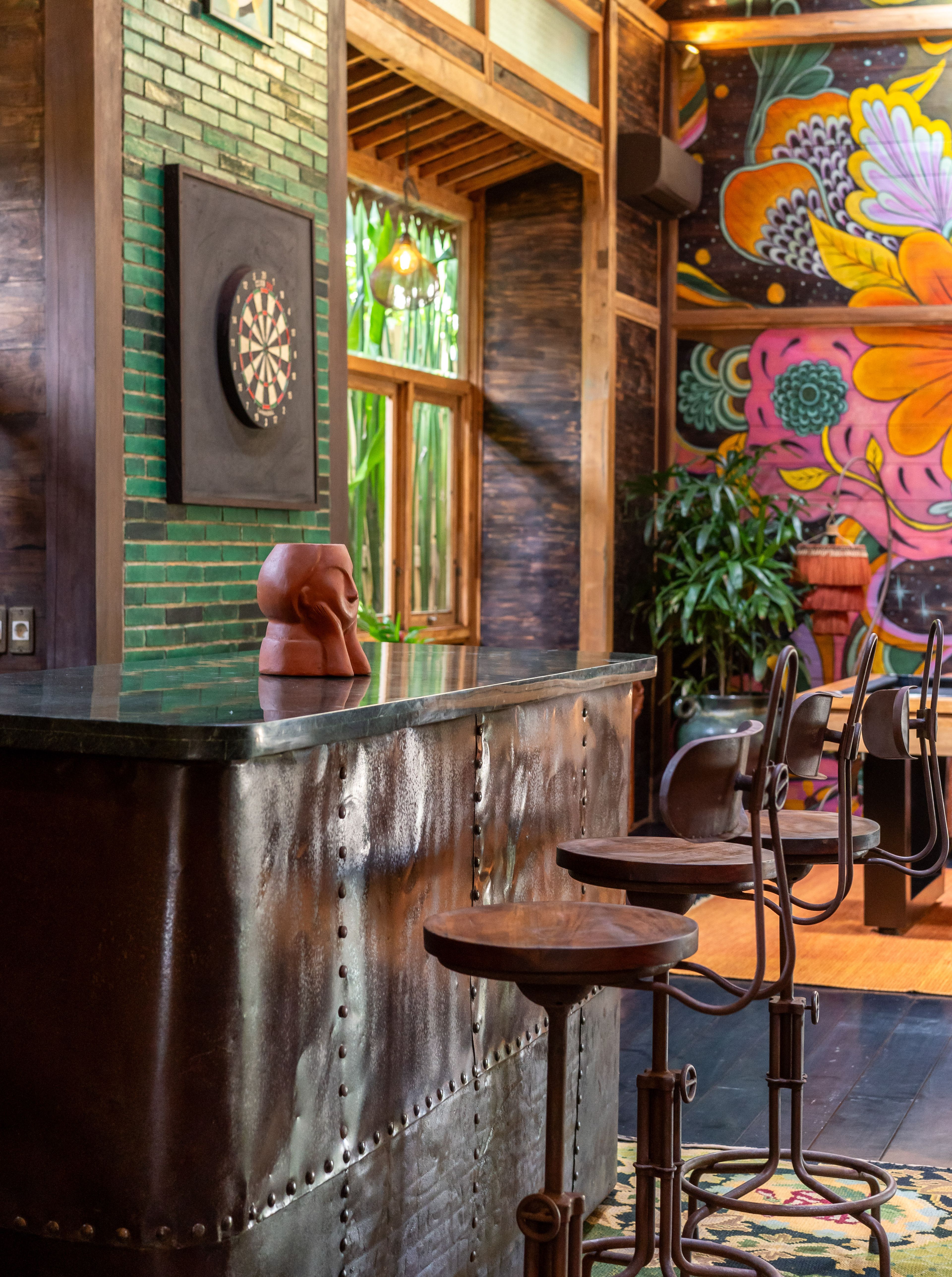The end of the bar with a carved figure on the counter, a dartboard on the brick wall and mural beyond.