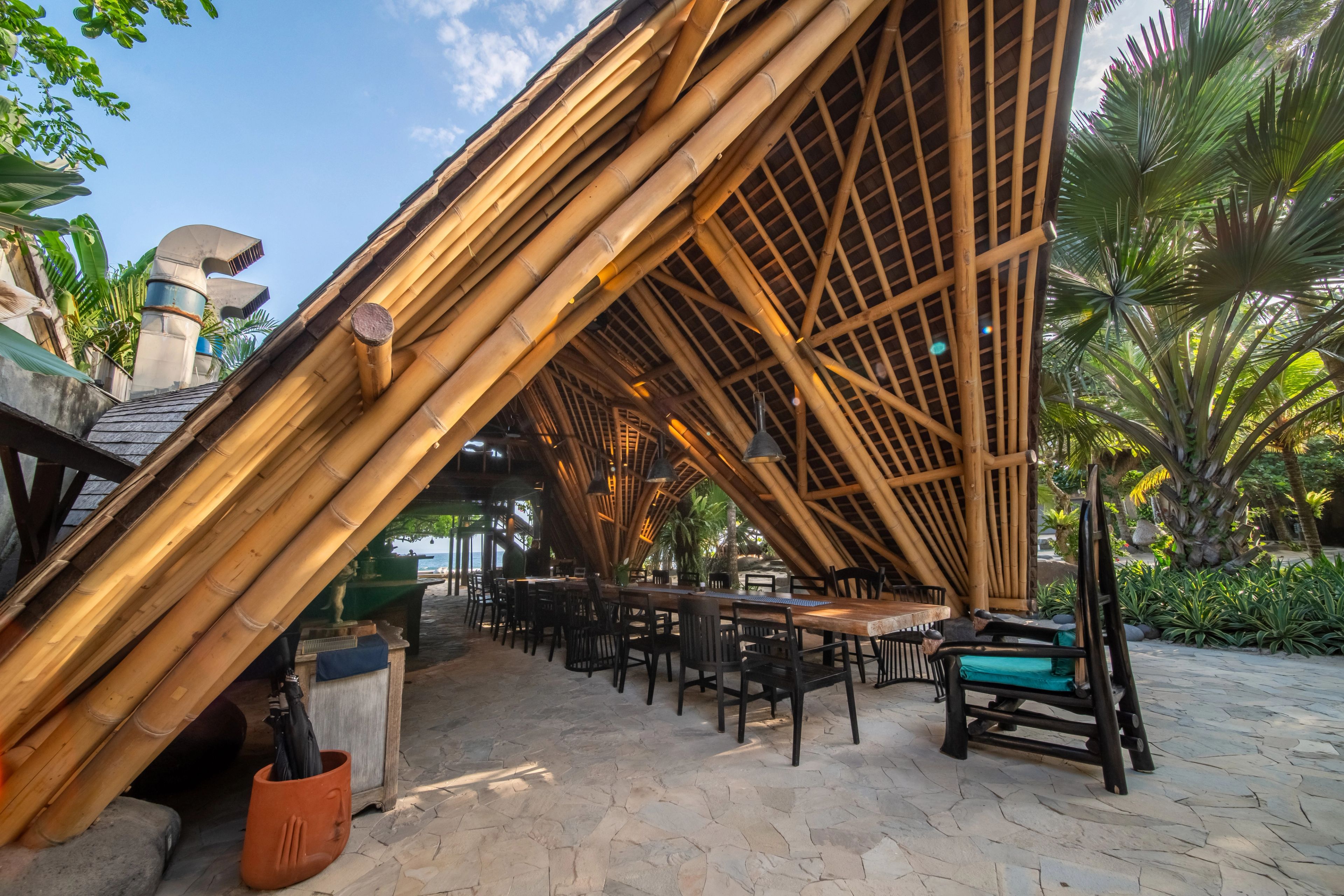 The splayed bamboo columns of the restaurant seen from outside, tables in the shade behind them.