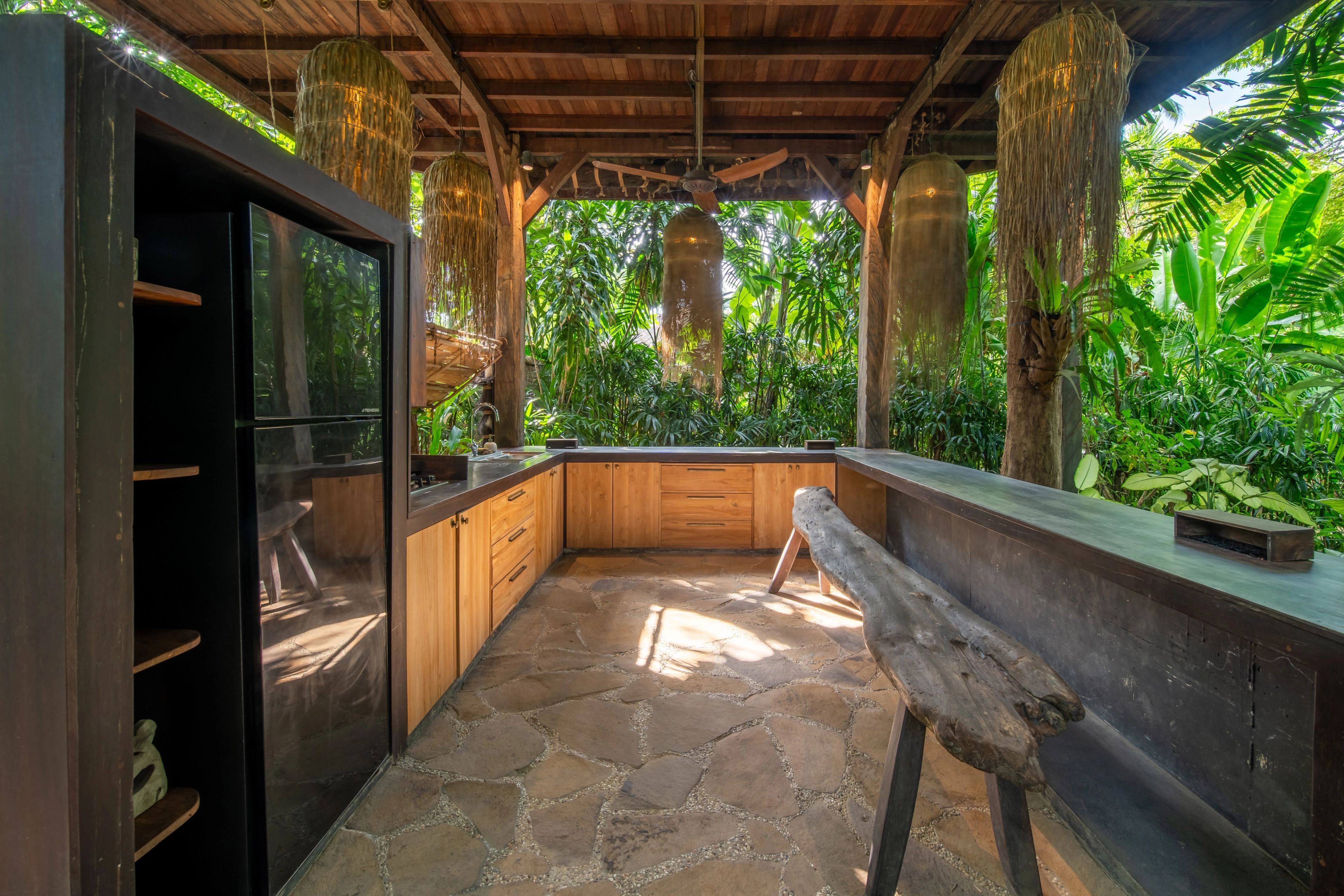 The length of the outdoor kitchen: timber cabinets, open shelving and a carved stool on the flagstones.