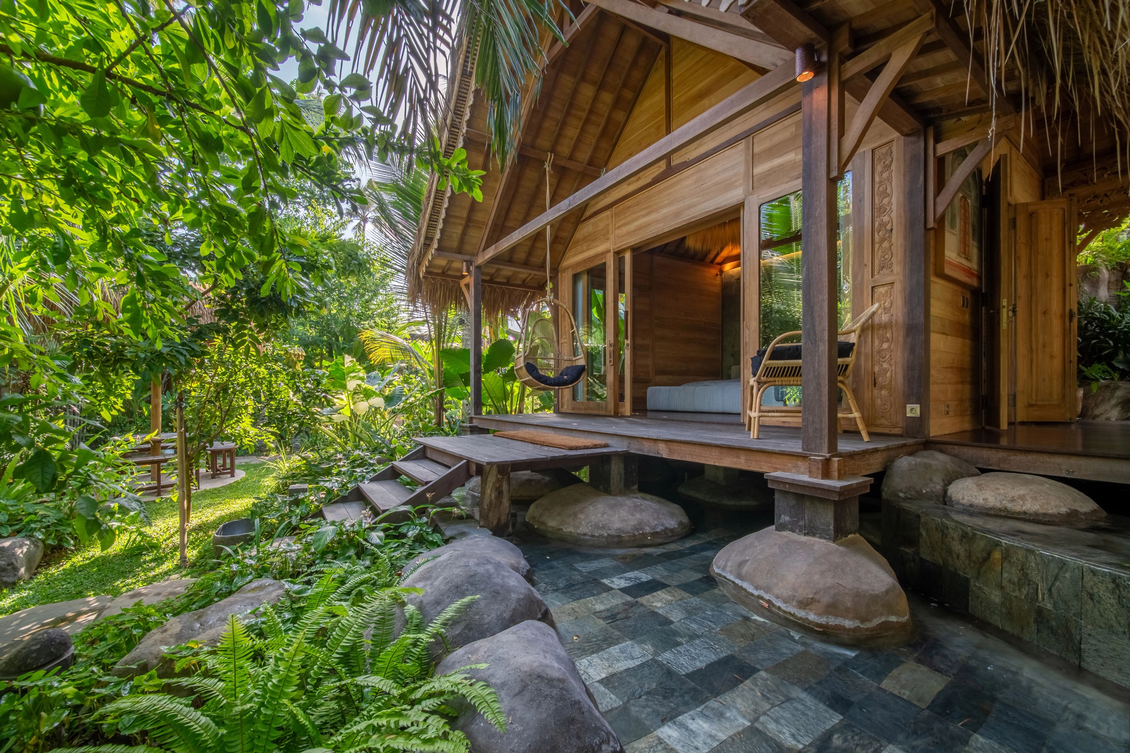The villa's deck and open doors seen from the garden, boulders set in the shallow pool below it.