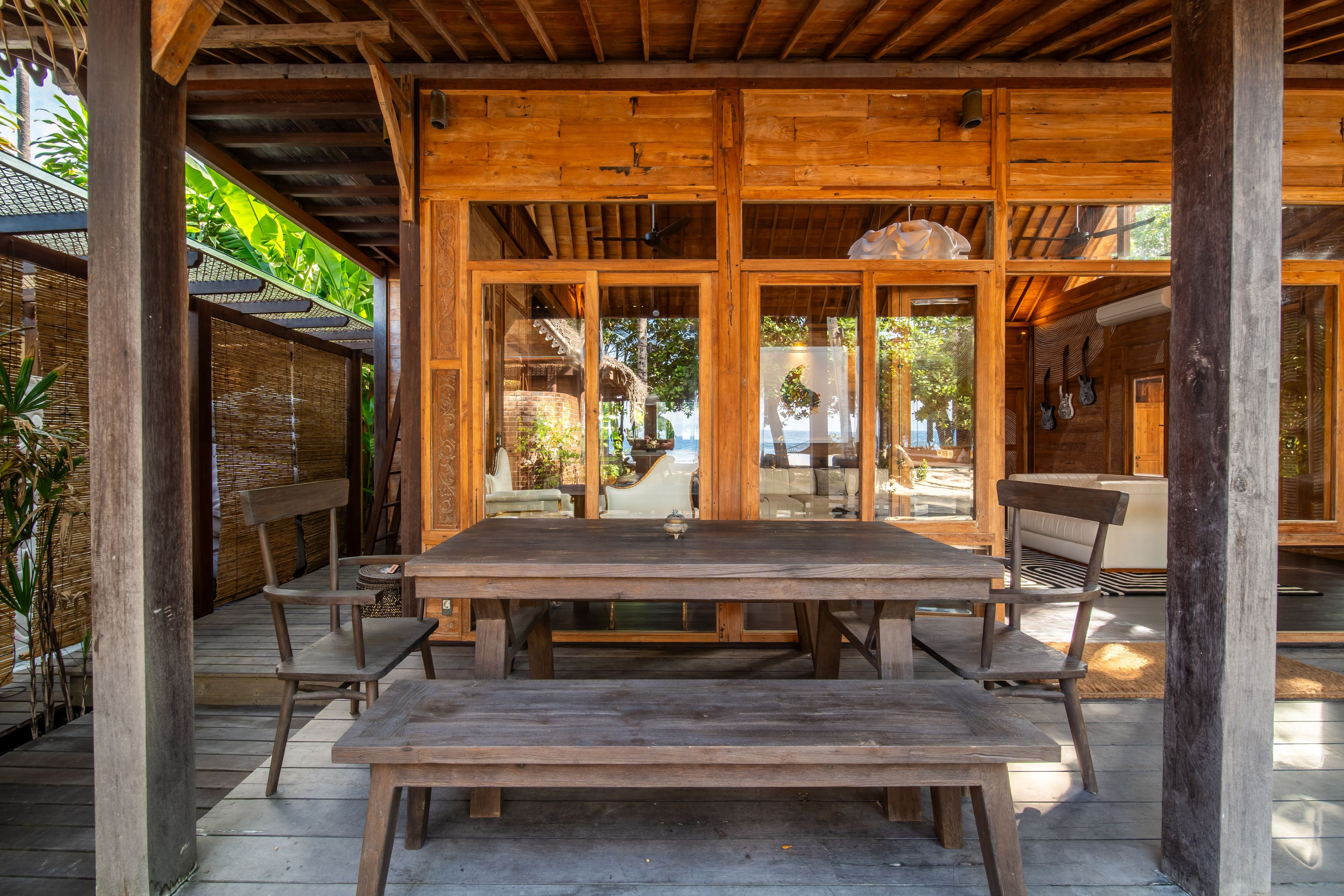 A long timber table and benches under the covered terrace, open to the courtyard.