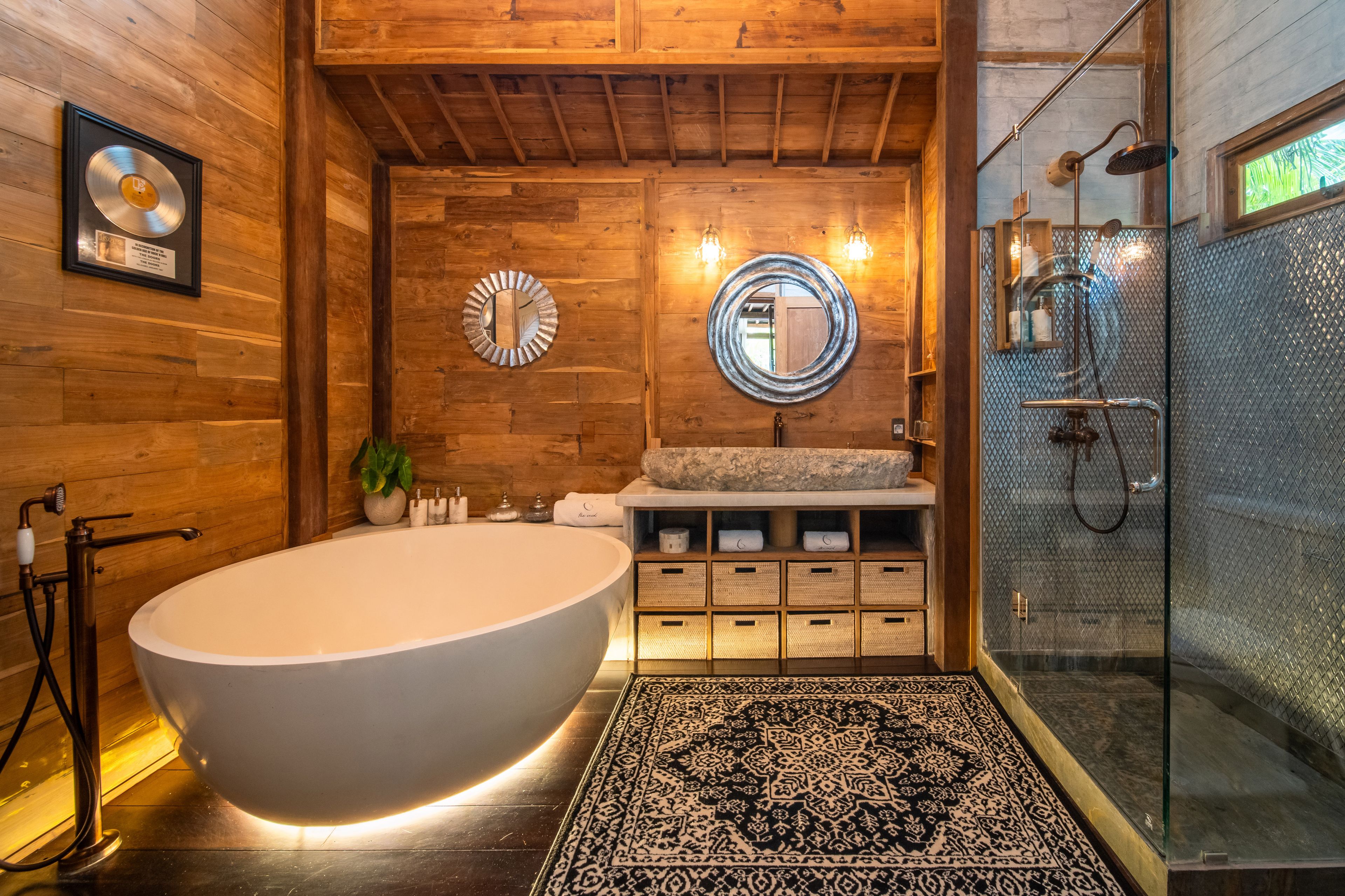 An oval freestanding bath on a patterned rug, glass shower alongside and a gold record on the wall.