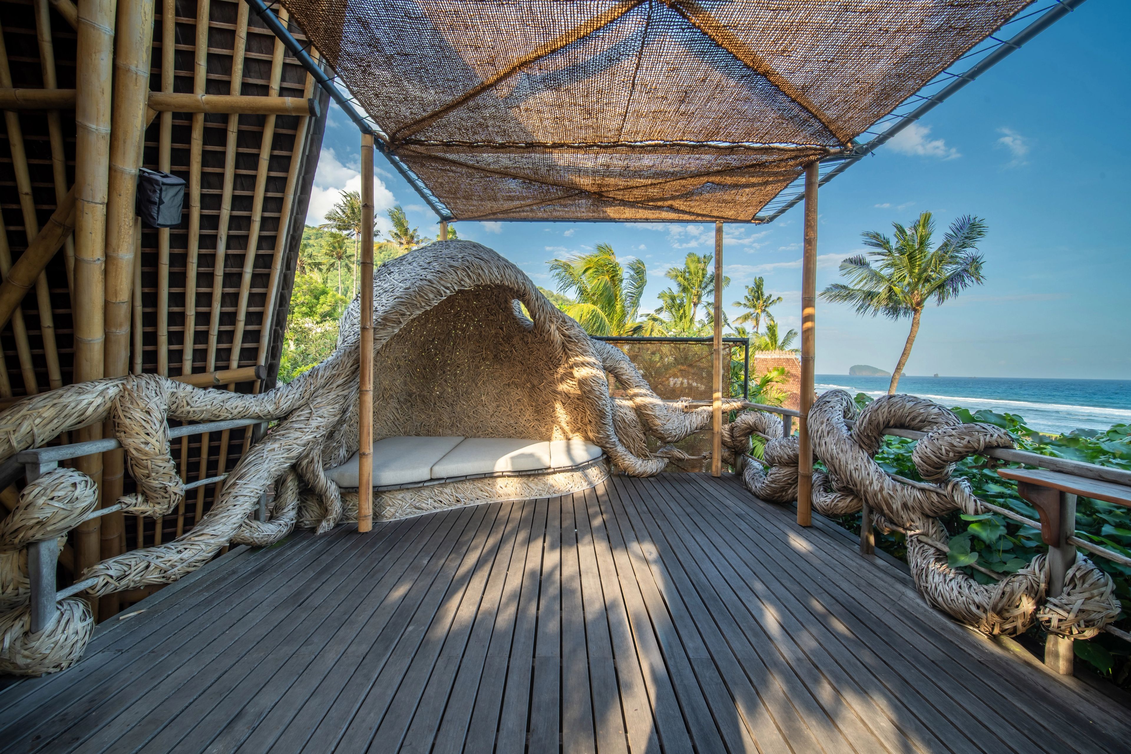 The woven cocoon nook framed by palm fronds, the ocean visible past the rail.