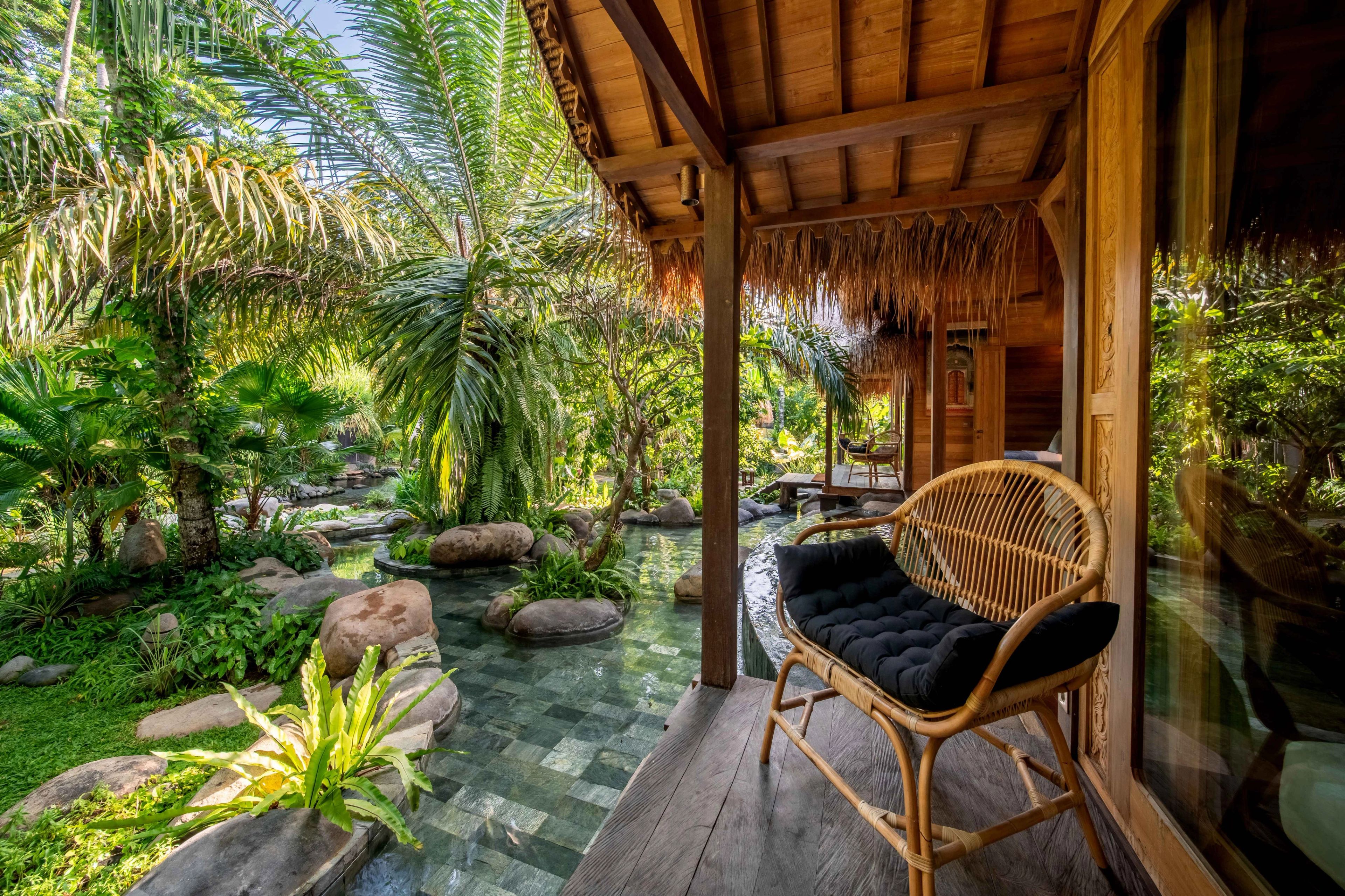 A cane rocking chair on the villa's deck, looking out over the pool and the planting.