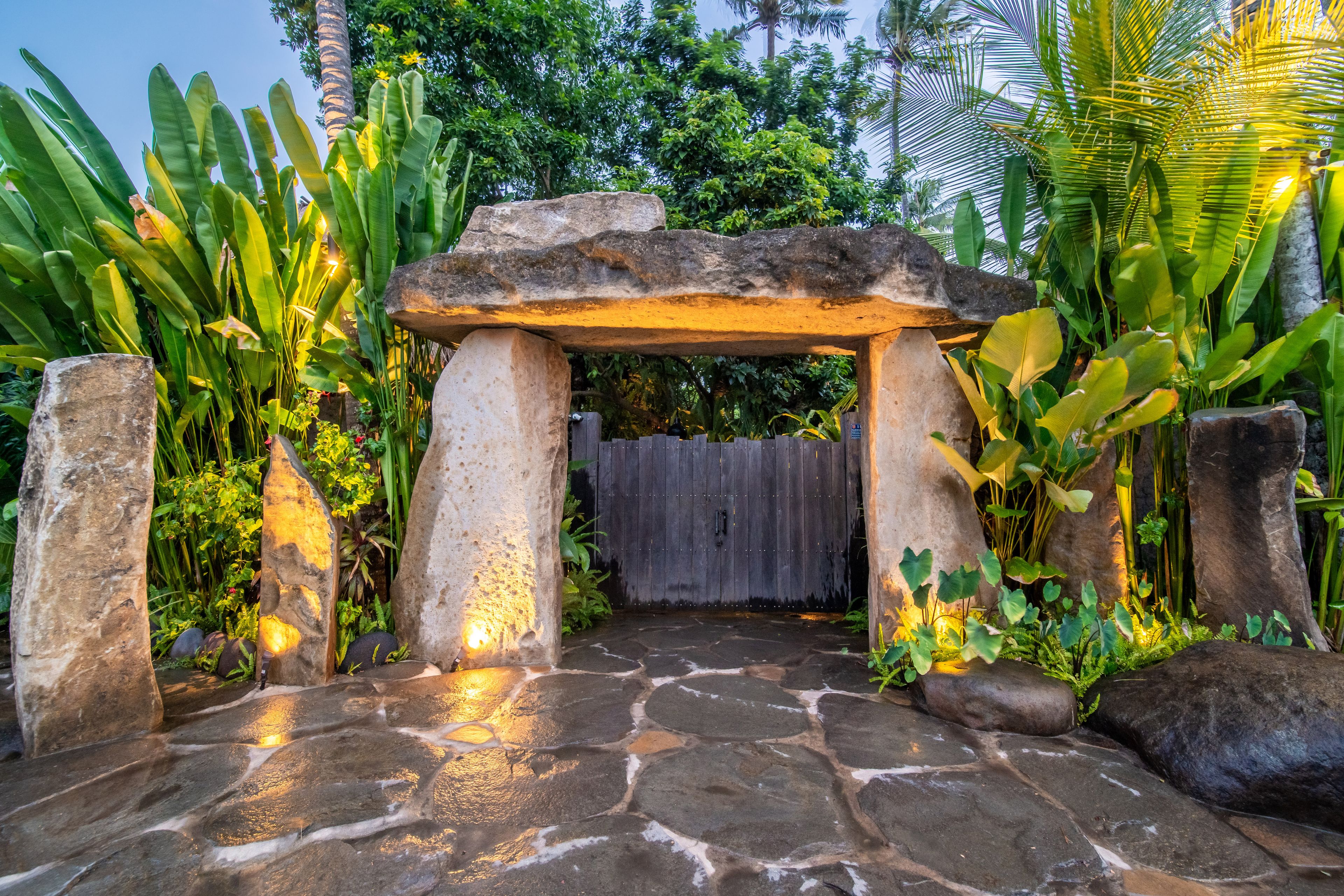 A megalithic stone gateway lit from below on a flagstone terrace, planting either side.