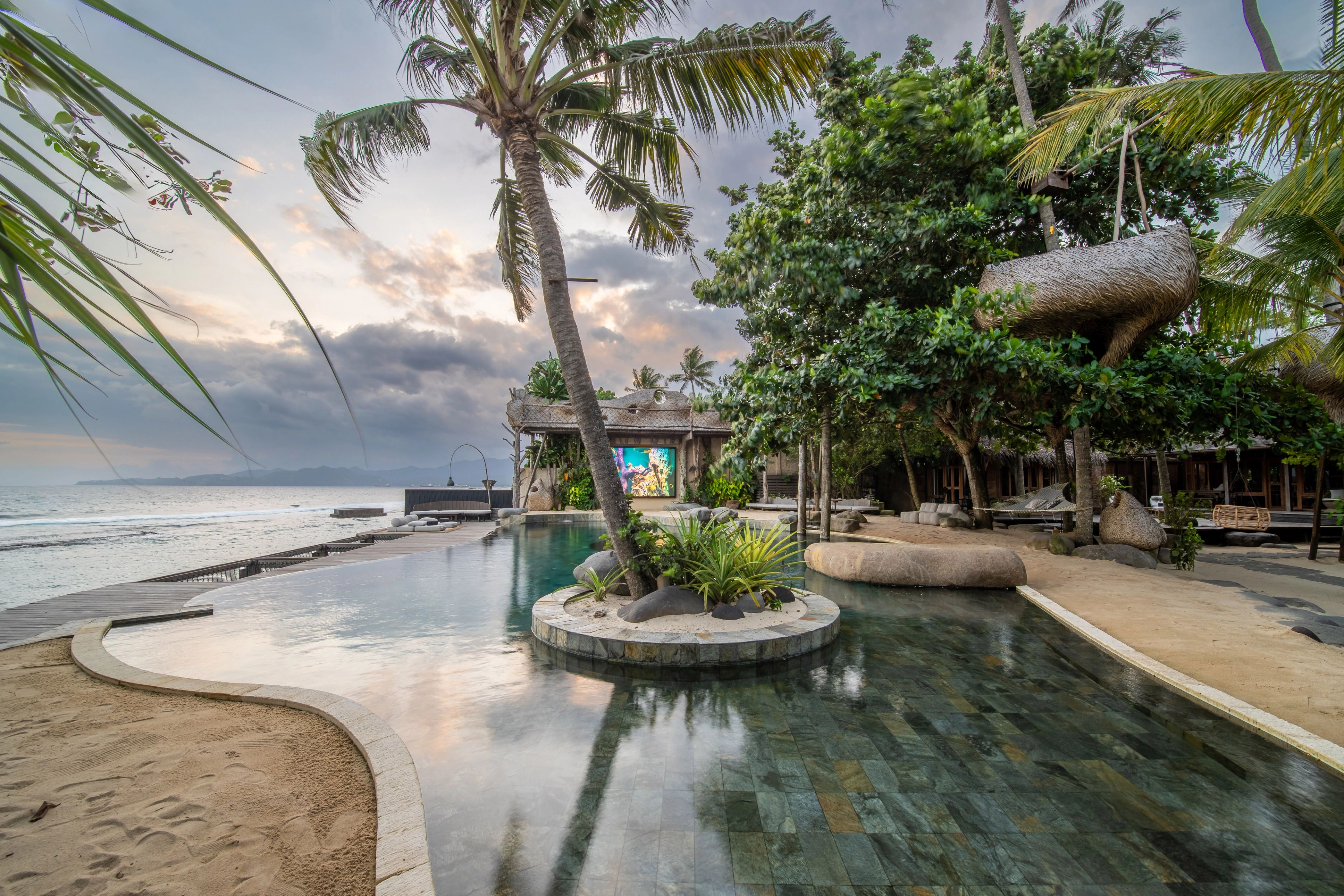 The pool and its planted island in early morning light, a nest pod hung in the trees behind.