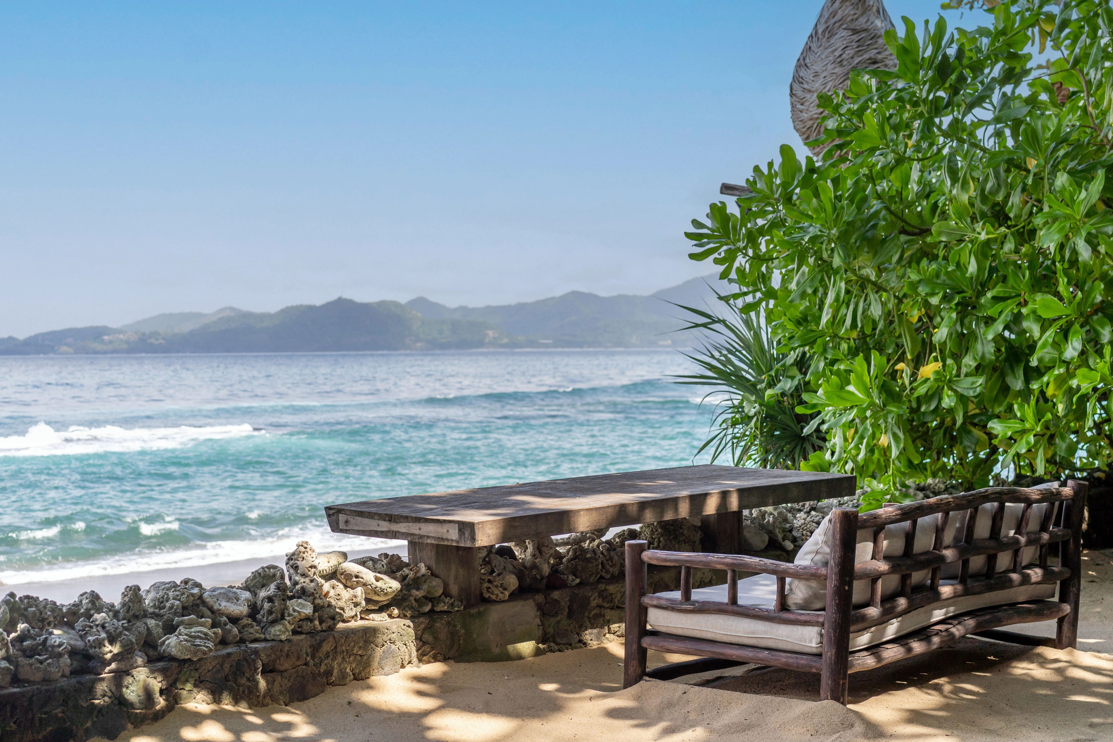 A curved black daybed on the coral stone terrace, looking out over the rocks to the sea.