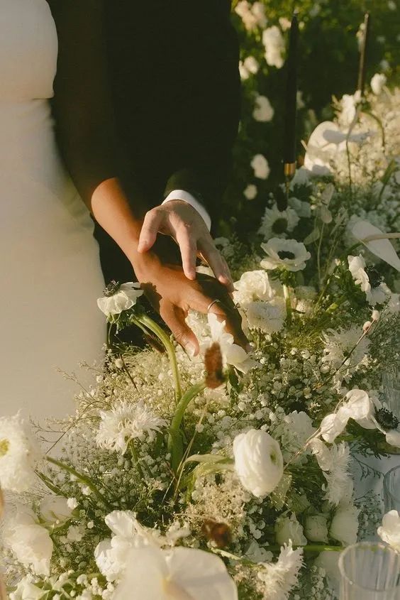 A hand reaching into a white arrangement of anemones, chrysanthemums and gypsophila.