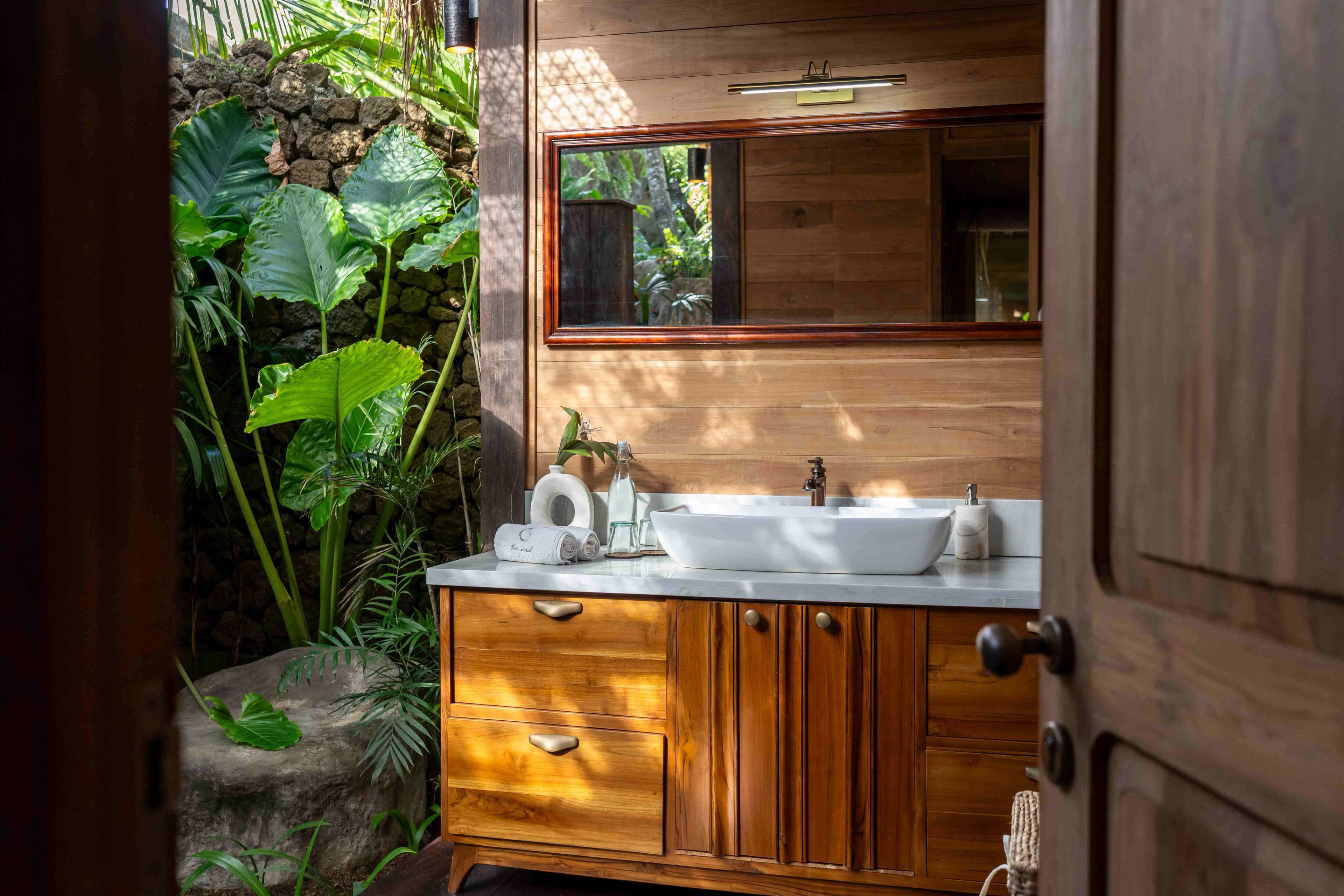 A stone basin on a timber vanity beside a window, with planting pressing up against the glass.