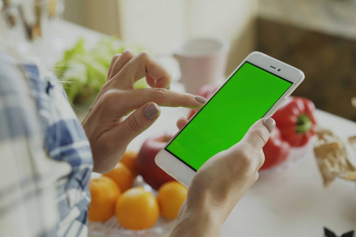 Person using a smartphone with a green screen.