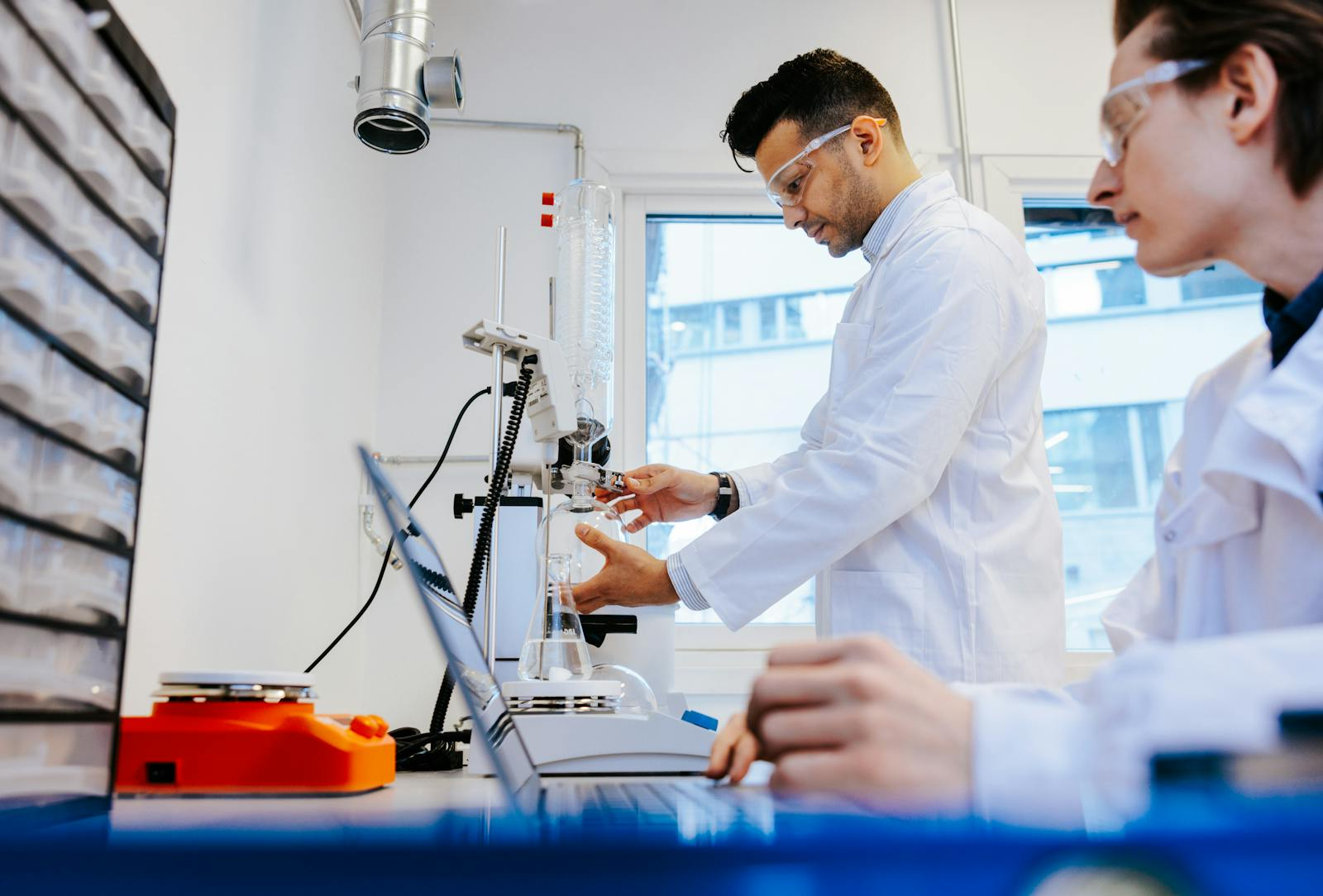 Scientists at the Photoncycle lab, wearing protective gear, conduct an experiment using laboratory glassware and digital tools.