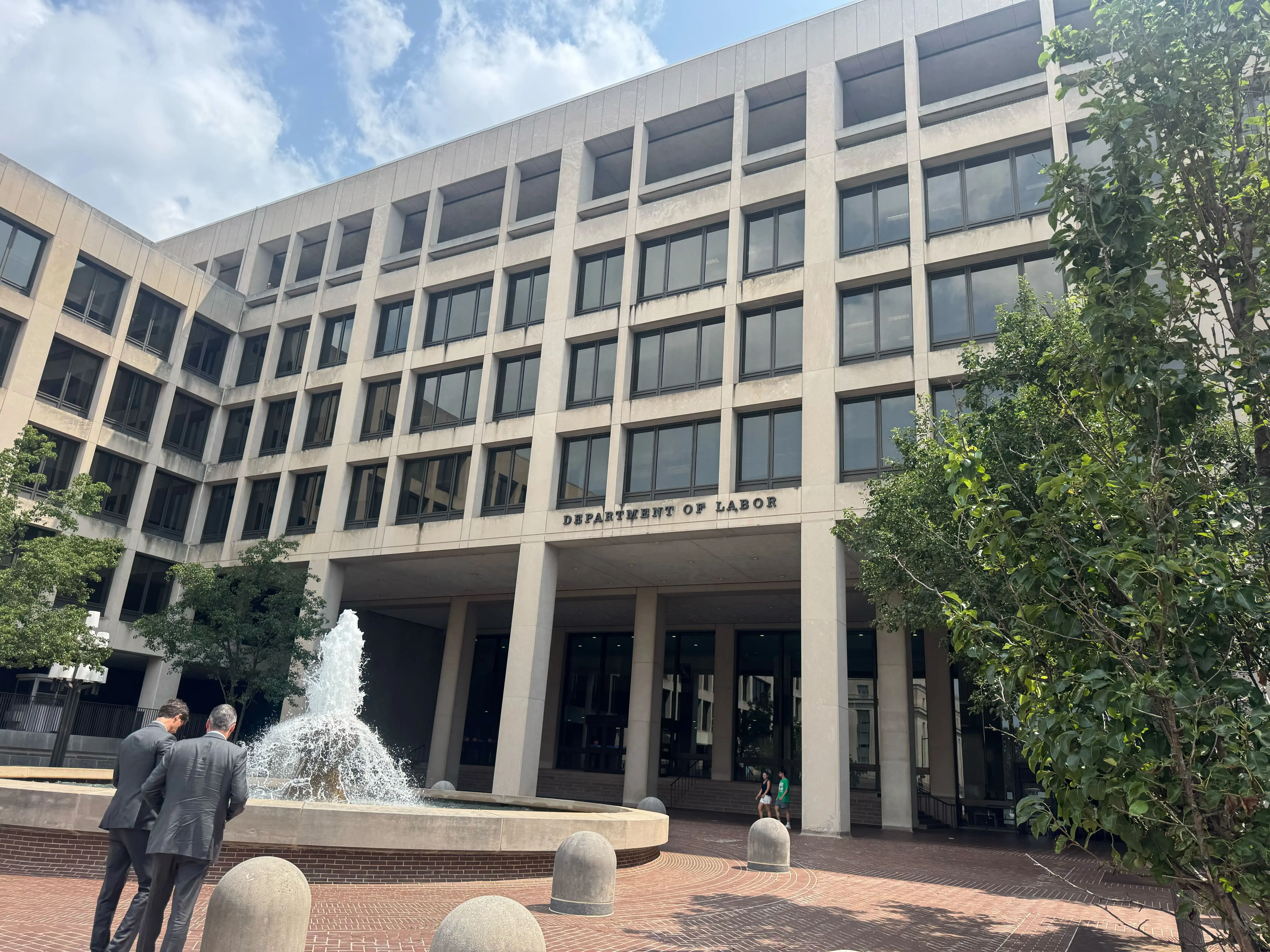 Picture of the entrance of the Department of Labor with two man in grey suit in front of the fountain in the entrance