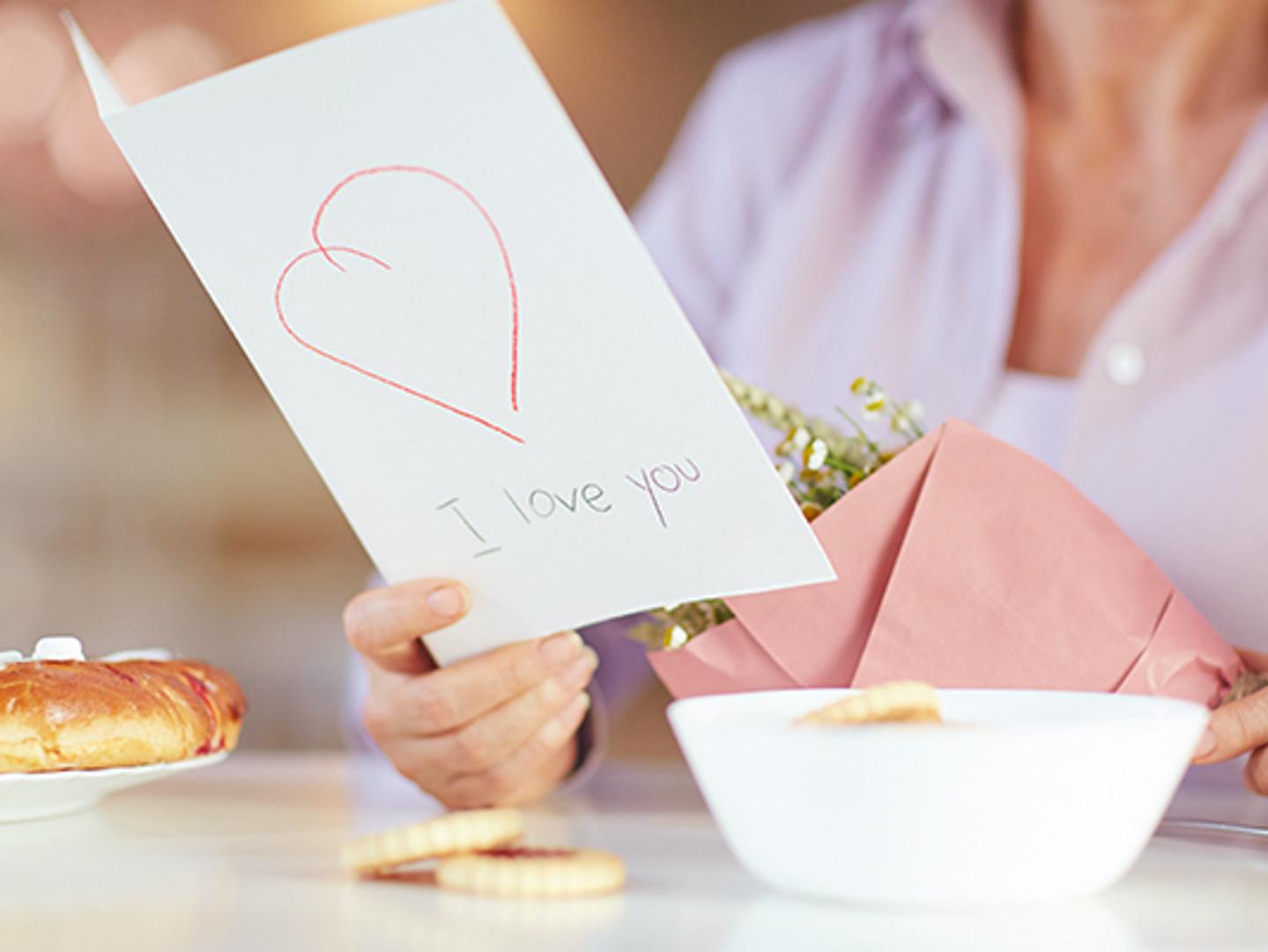 a woman is holding a bouquet of flowers and a card that says `` i love you '' .