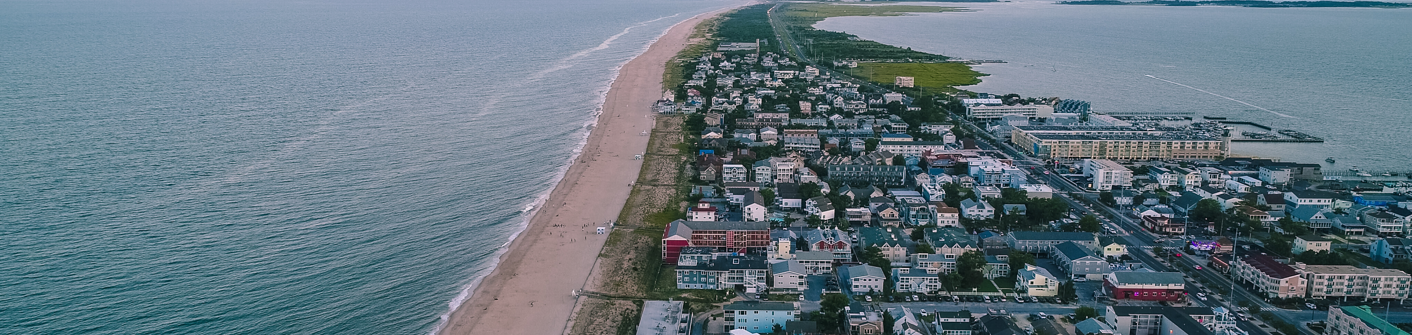 A long stretch of beach in closeup with a blurred background of coastal homes and the vast ocean extending into the horizon in Rehoboth Beach, Delaware.