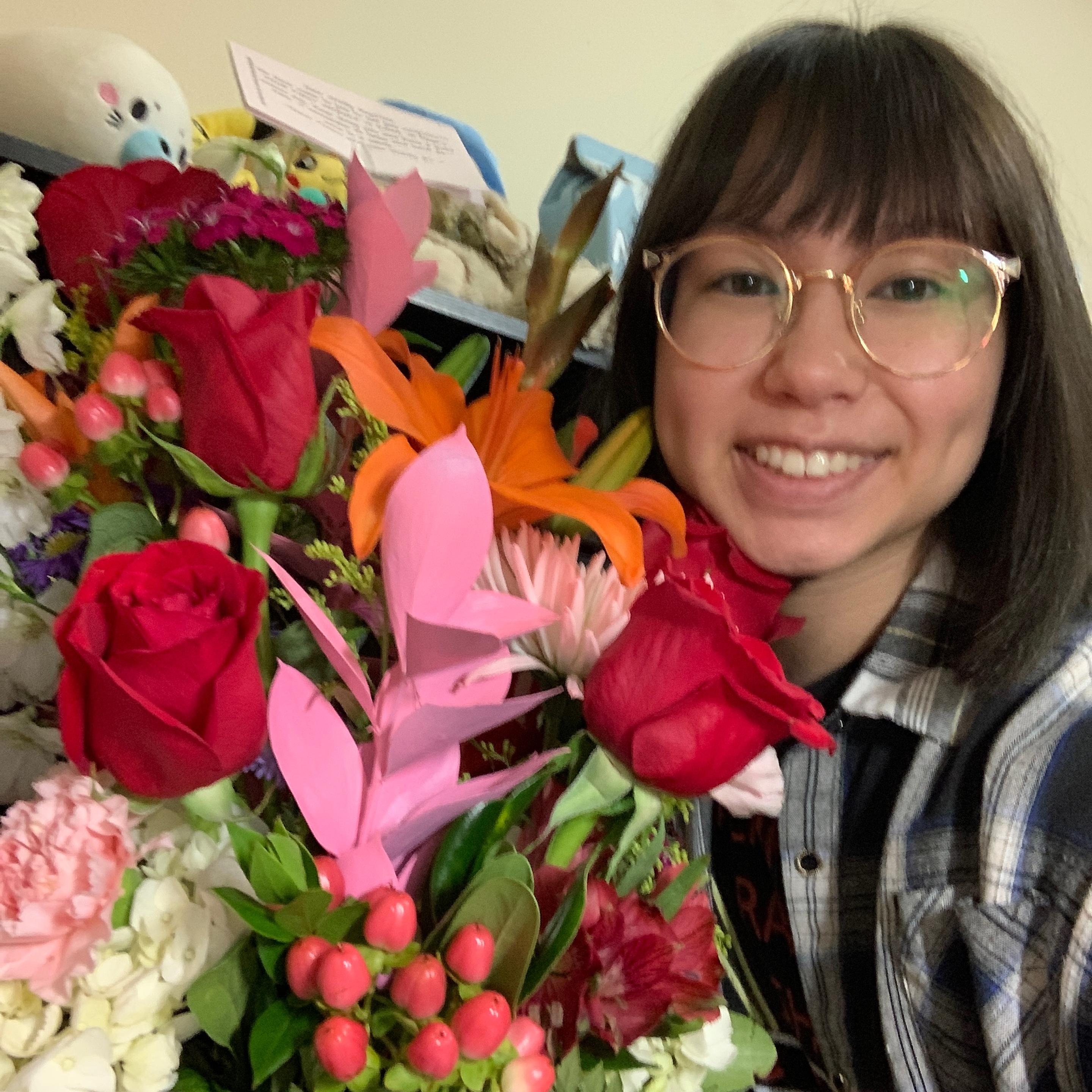 Woman with glasses next to a big floral arrangement with pink and red flowers