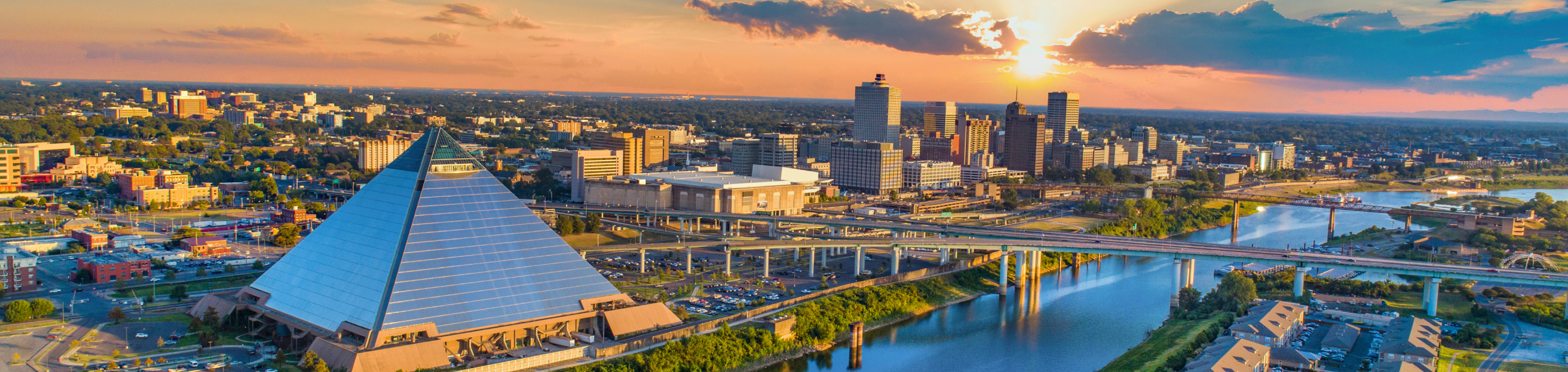 The Memphis skyline in closeup with a blurred background of the Bass Pro Shops Pyramid and the Mississippi River under a sunset in Tennessee.