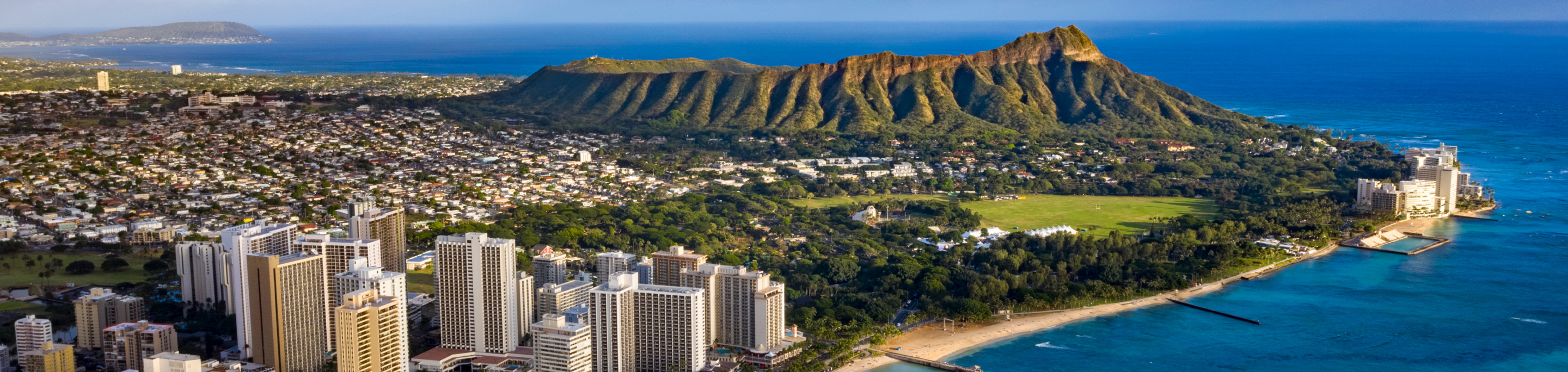 Diamond Head crater in closeup with a blurred background of Waikiki Beach's high-rise buildings and the turquoise waters of the Pacific Ocean in Honolulu, Hawaii.