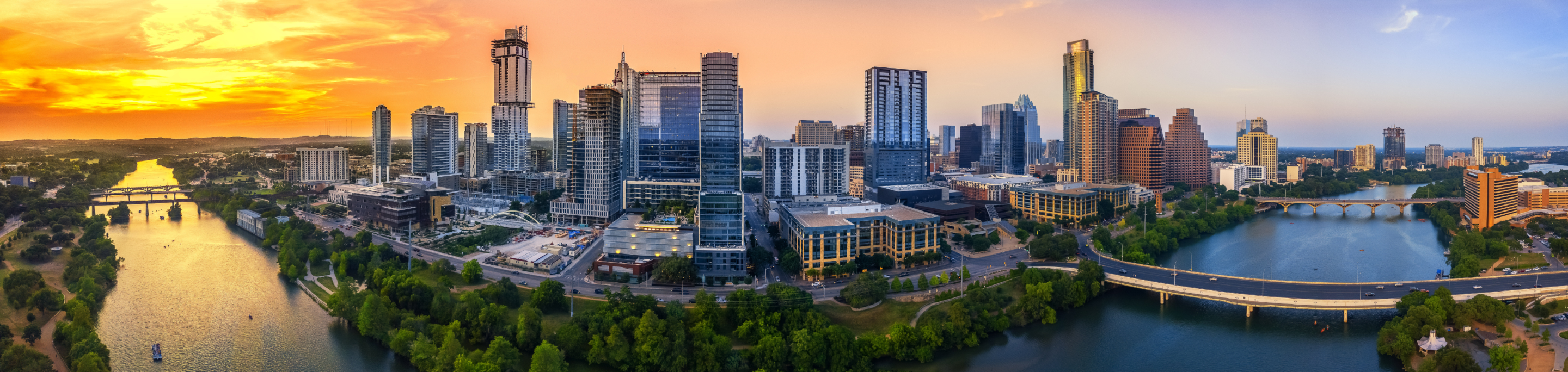 The Austin skyline in closeup with a blurred background of modern skyscrapers lining the banks of the Colorado River, under a vibrant sunset sky in Texas.