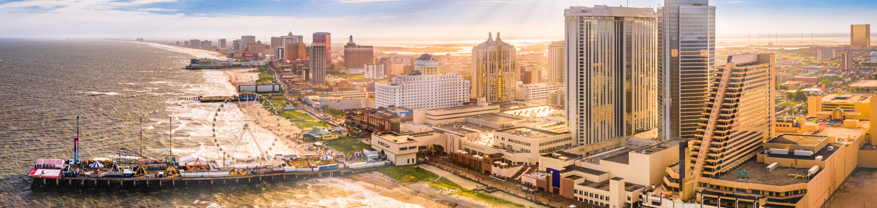 The Atlantic City skyline in closeup with a blurred background of casinos, a Ferris wheel on the pier, and the expansive shoreline under golden sunlight in New Jersey.