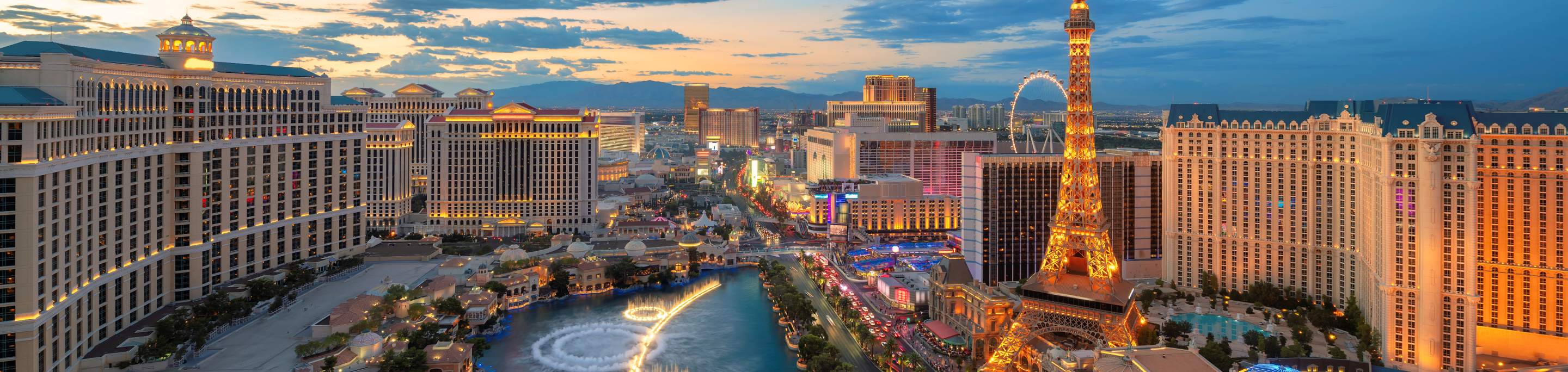 The Las Vegas Strip in closeup with a blurred background of iconic hotels, casinos, and the Eiffel Tower replica illuminated at dusk in Nevada.