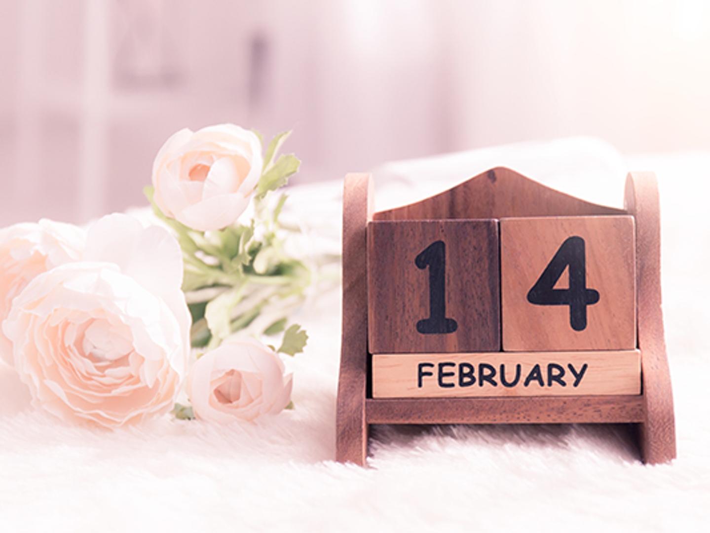 a wooden calendar with the date of february 14 next to a bouquet of flowers .