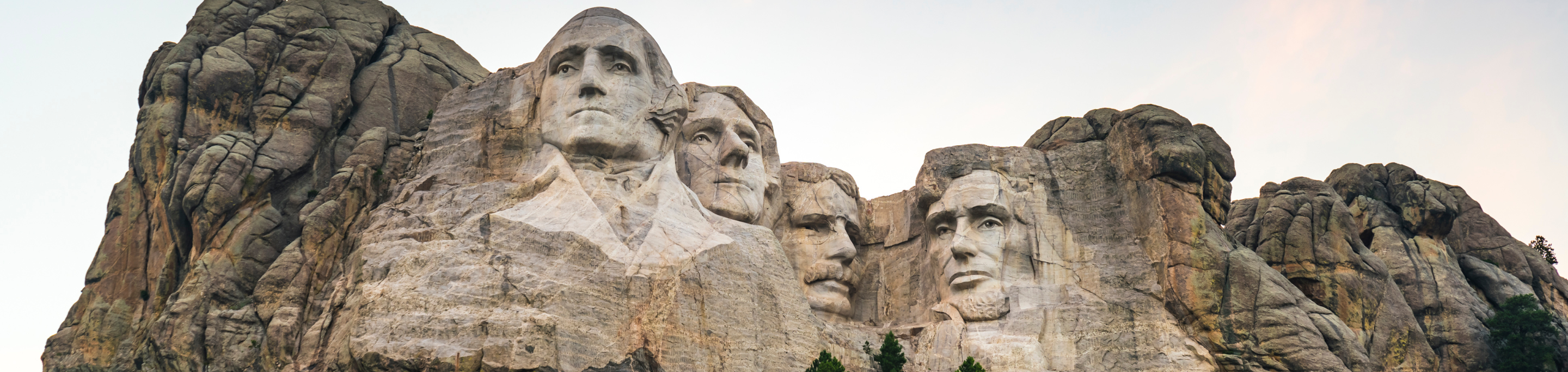 The iconic Mount Rushmore in closeup with a blurred background of rugged granite cliffs, showcasing the carved faces of four U.S. presidents against the backdrop of a clear sky in South Dakota.