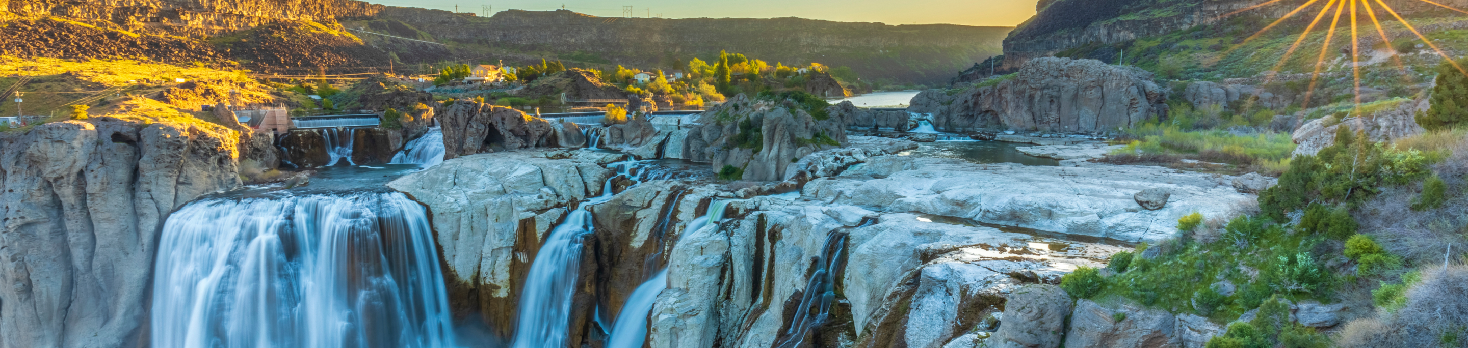 Shoshone Falls cascading in closeup with a blurred background of rugged cliffs and the Snake River under a glowing sunset in Twin Falls, Idaho.