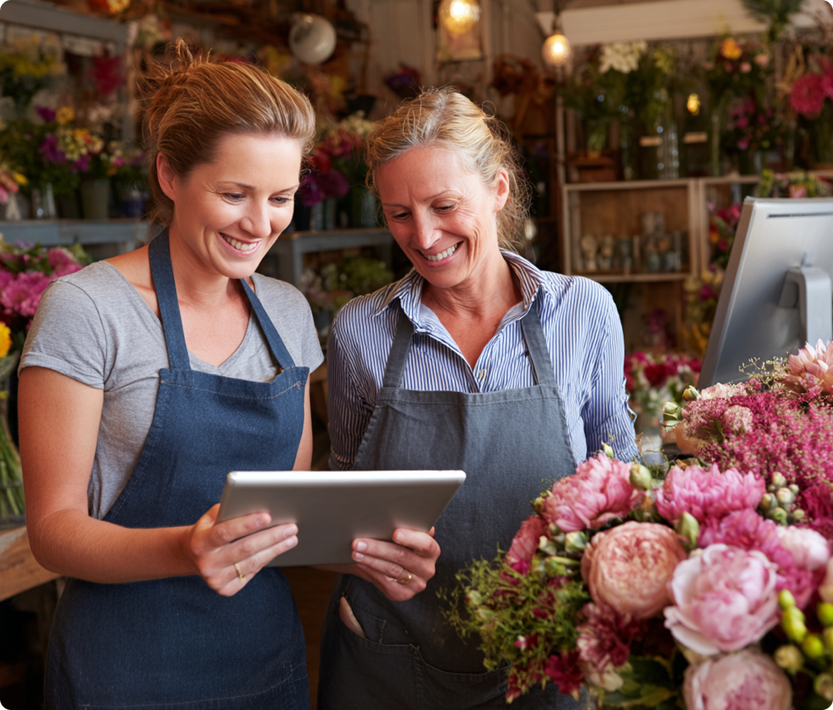 Two smiling florists looking at a tablet in a flower shop.