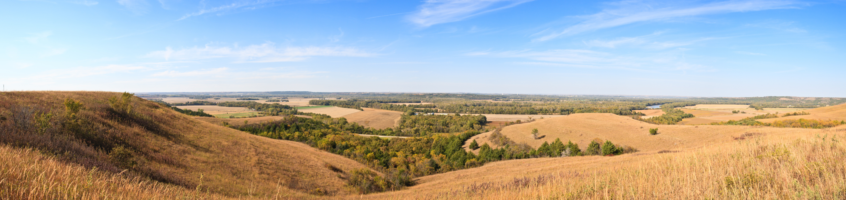 Rolling hills and open plains in closeup with a blurred background of expansive farmland and a clear blue sky in the Flint Hills region of Kansas.