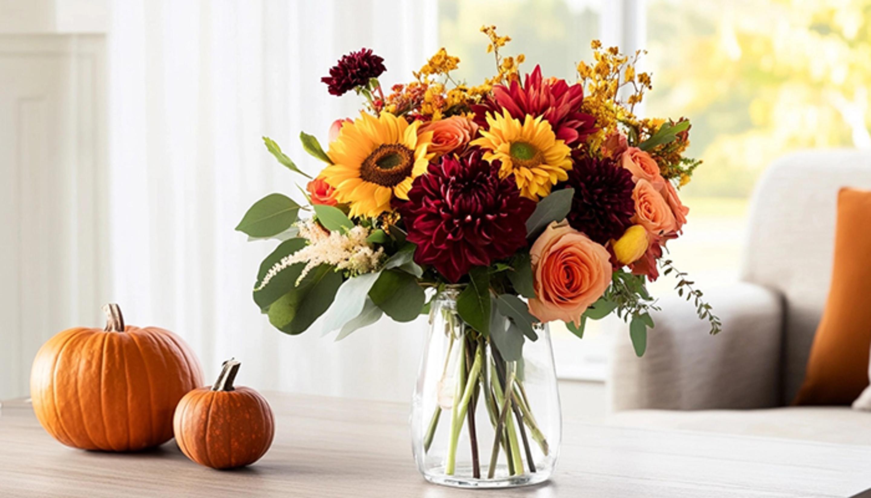 A vase filled with fall flowers is sitting on a table next to pumpkins.