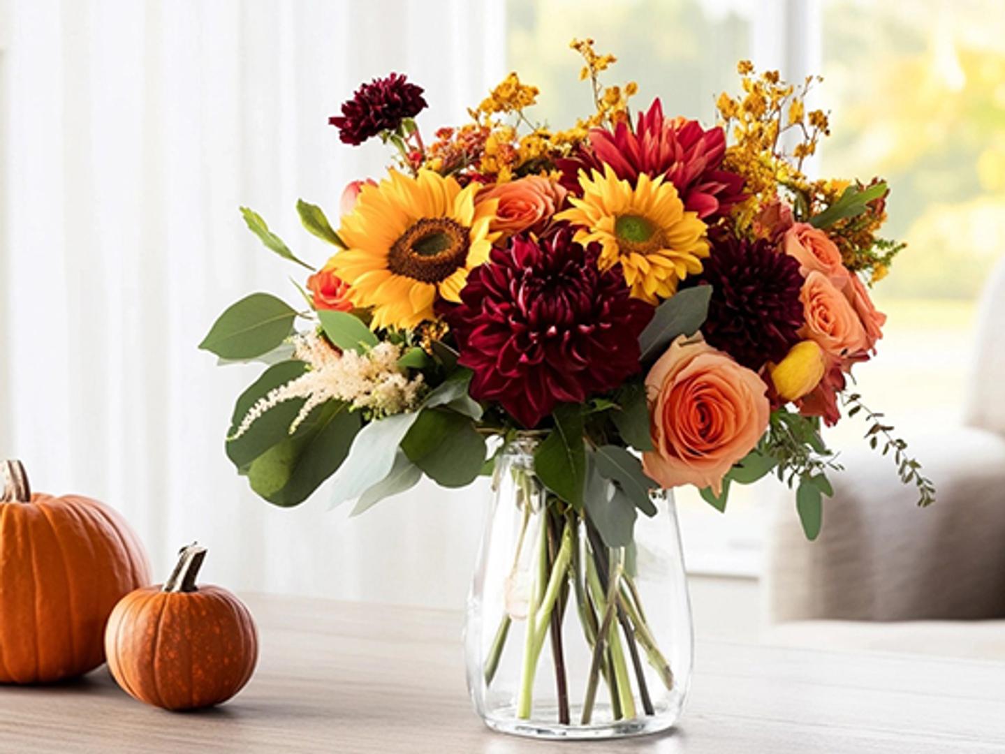 a vase filled with flowers is sitting on a table next to pumpkins.