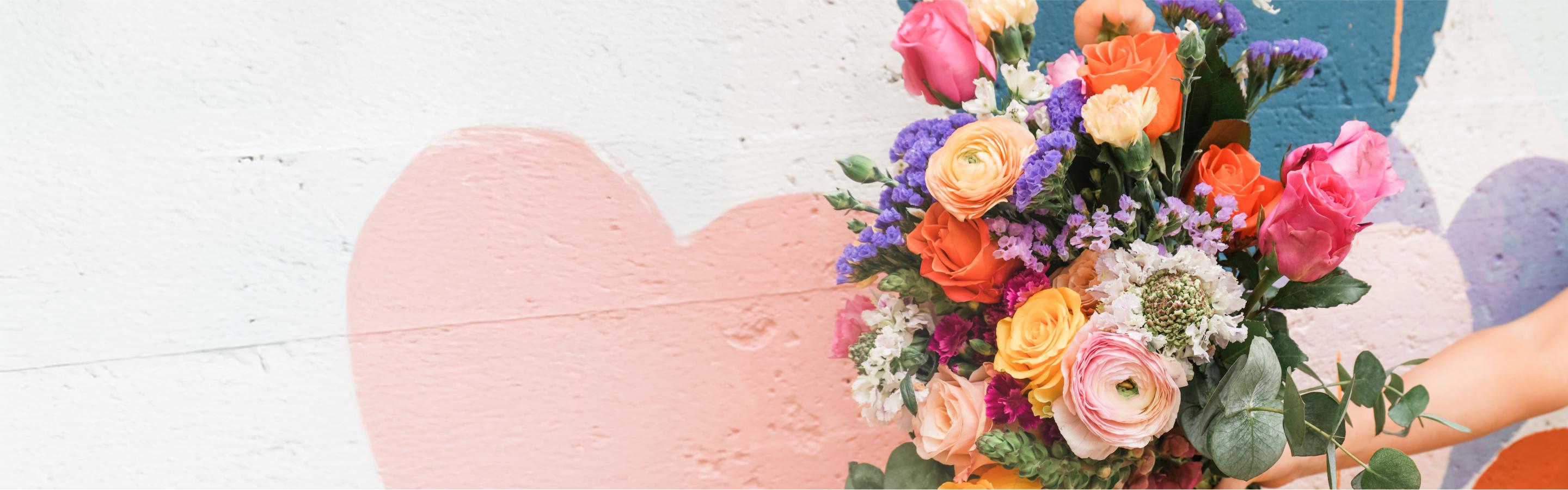 a person is holding a bouquet of flowers in front of a wall with a heart painted on it .