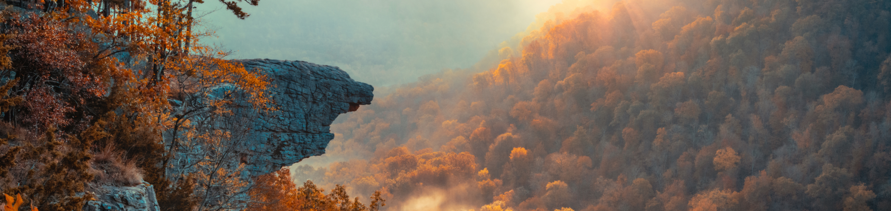 A rocky outcrop in closeup with a blurred background of a sunlit autumn forest in the Ozark Mountains, Arkansas.