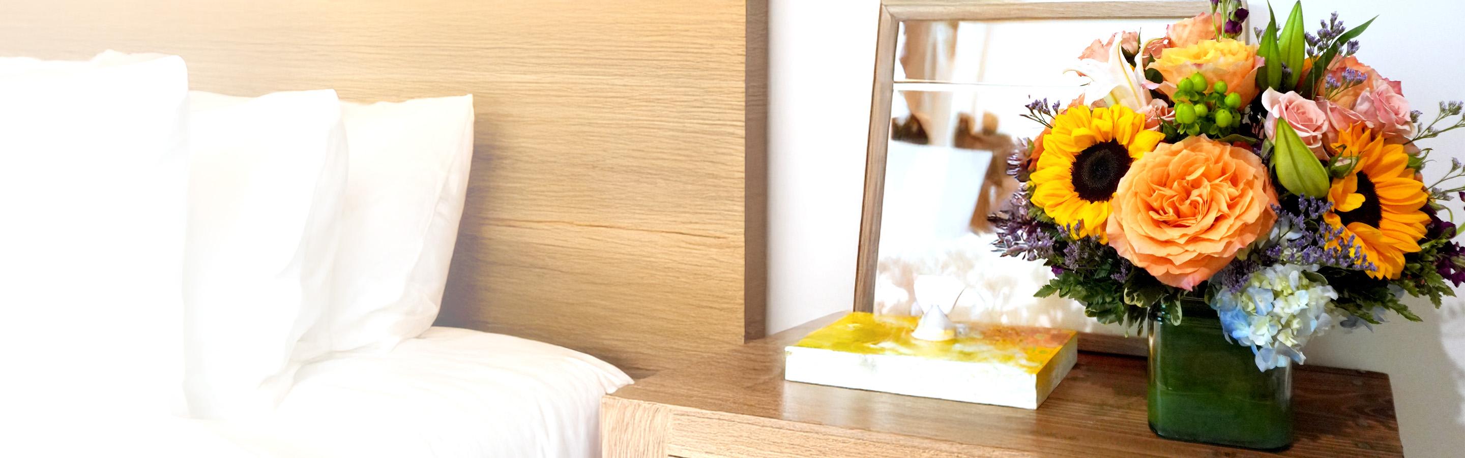 a vase of flowers is sitting on a nightstand next to a bed .
