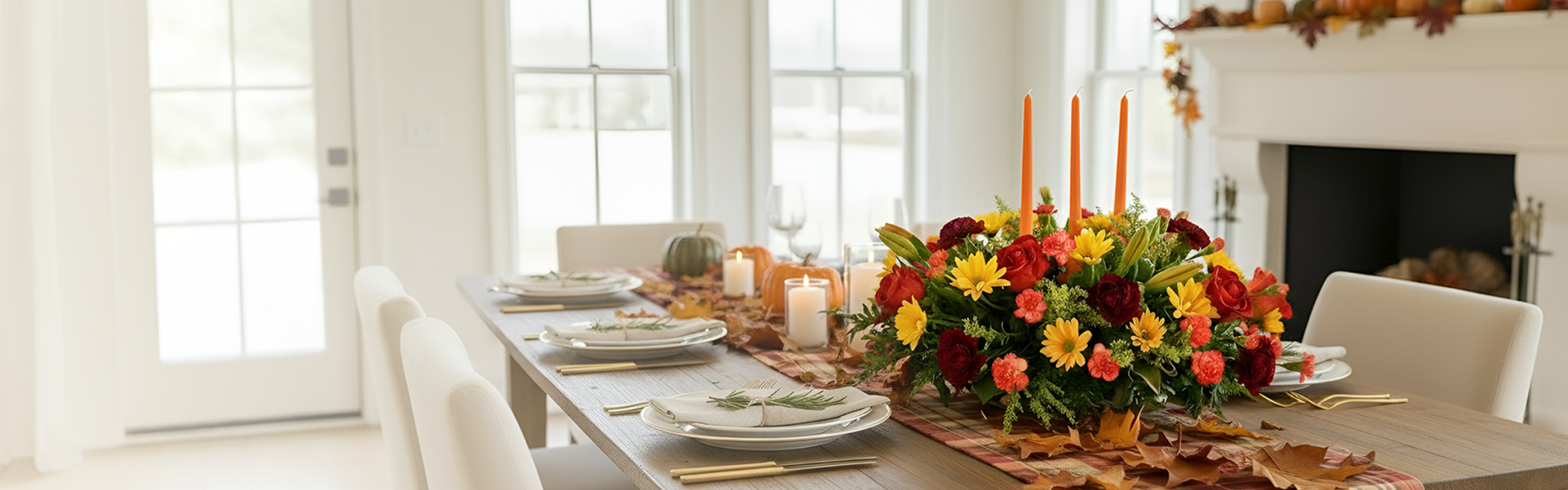 Autumnal dining table set with a vibrant floral centerpiece, candles, pumpkins, and place settings on a plaid runner.