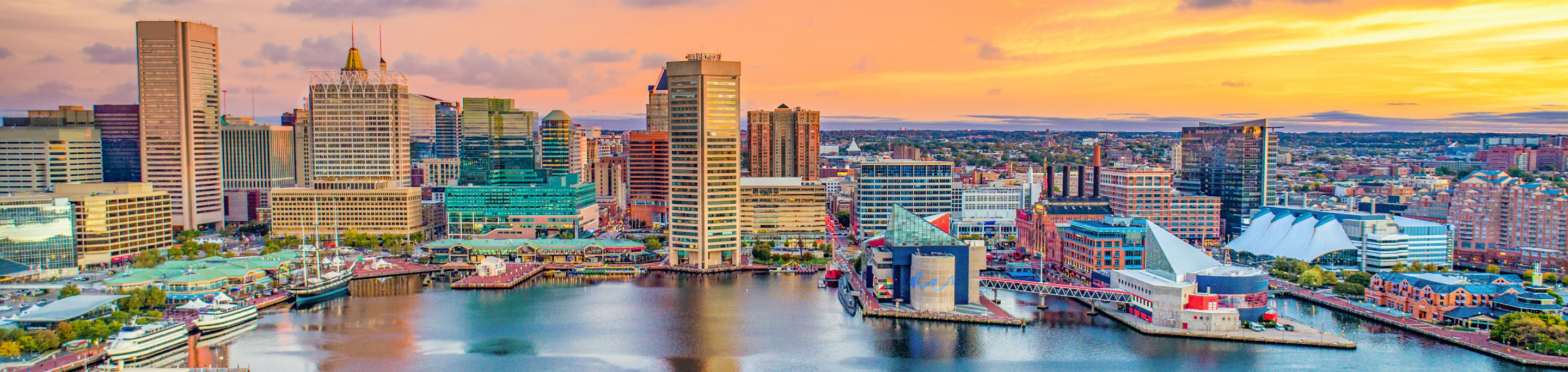 The Baltimore Inner Harbor in closeup with a blurred background of the city's skyline under a colorful sunset in Maryland.