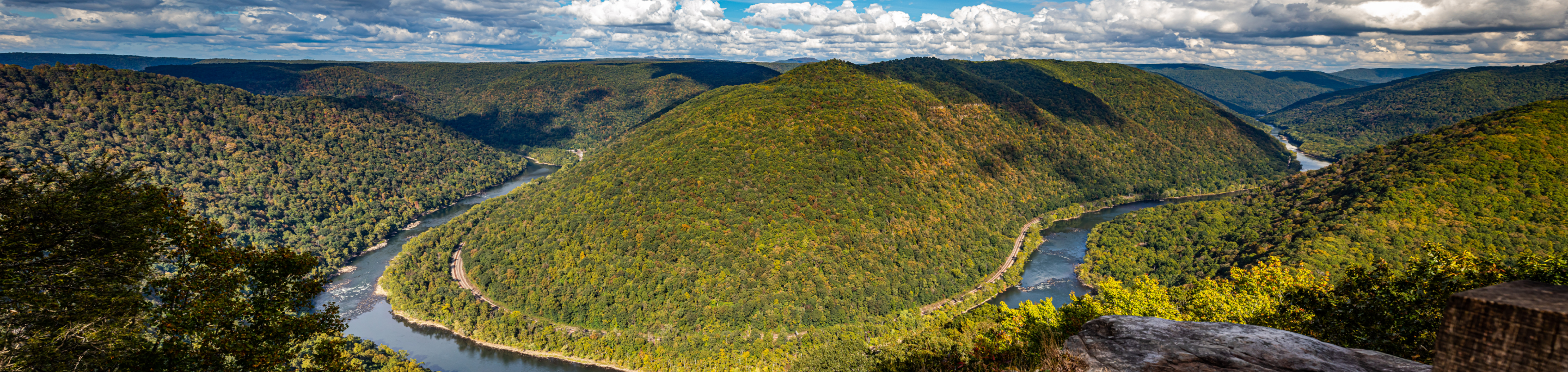 The New River Gorge in closeup with a blurred background of rolling, tree-covered mountains under a sky filled with fluffy clouds in West Virginia.