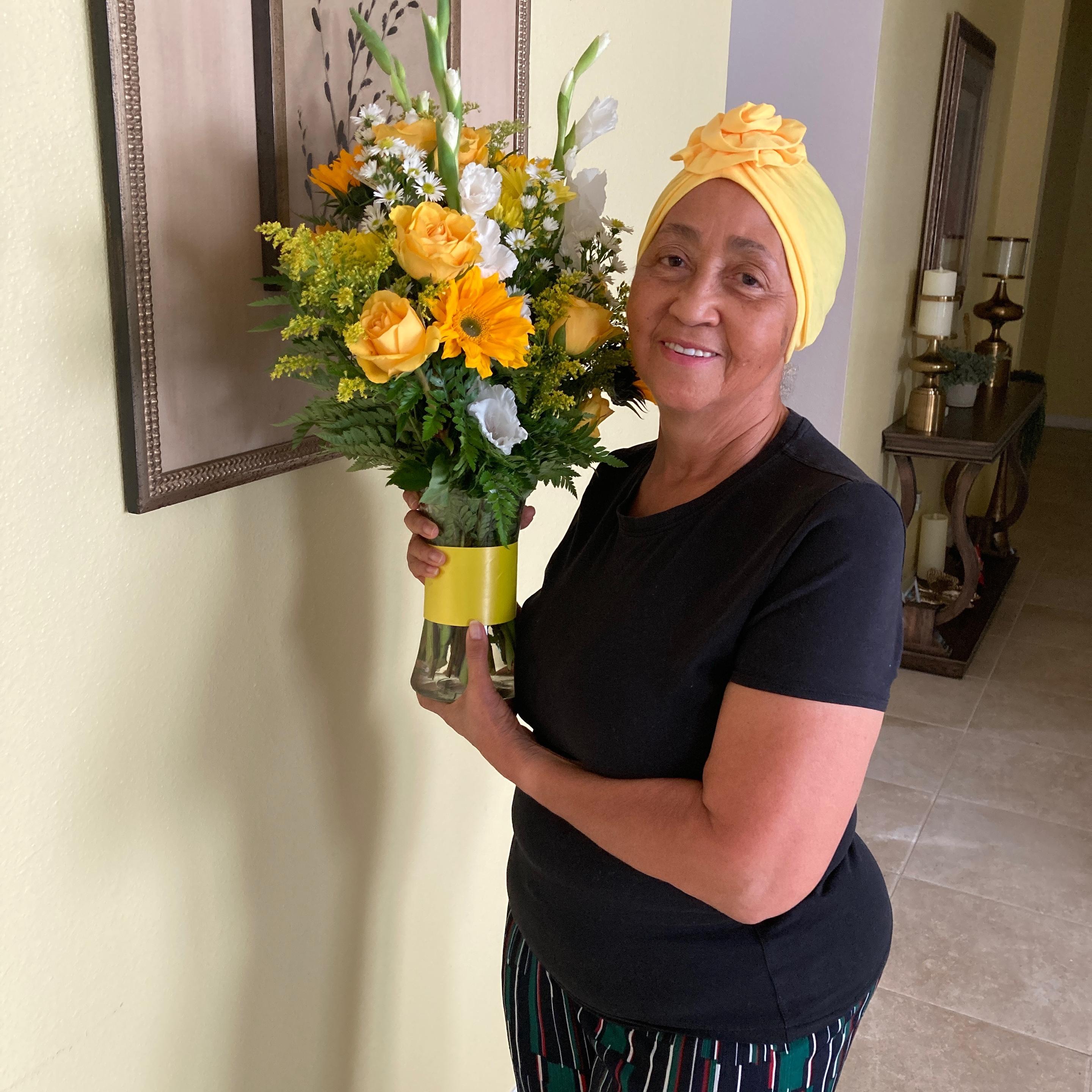 Woman holding a beautiful flower arrangement in a clear vase with yellow flowers