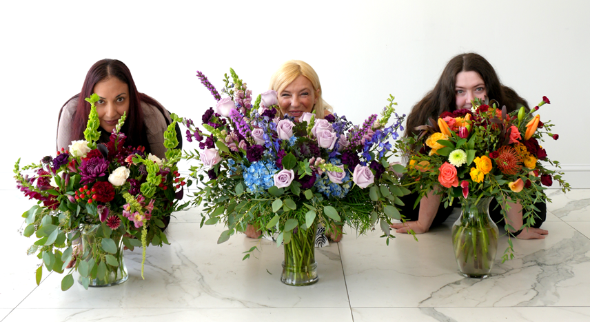 three women laying on the floor with vases of fall flowers in front of them